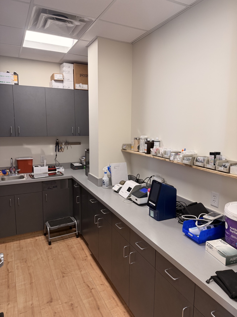 Laboratory corner with cabinets, countertop, and shelves holding lab supplies, with a small step stool on the floor.
