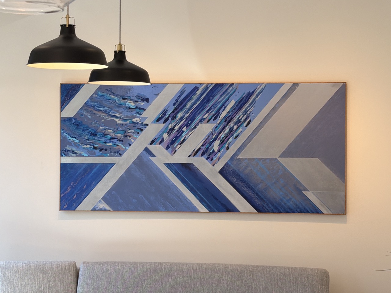 Blue abstract painting with geometric shapes hanging above a beige sofa.