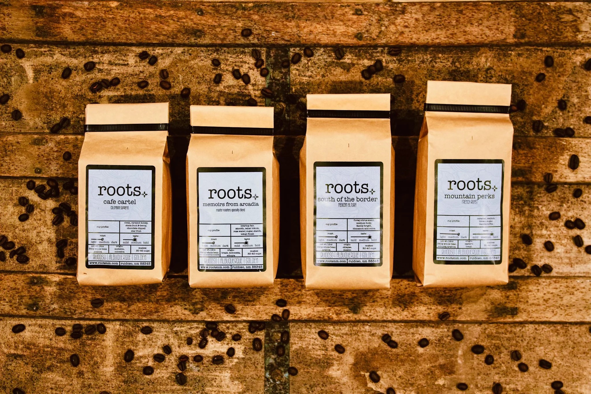 Four brown paper bags with white labels arranged on a wooden surface with black dots.