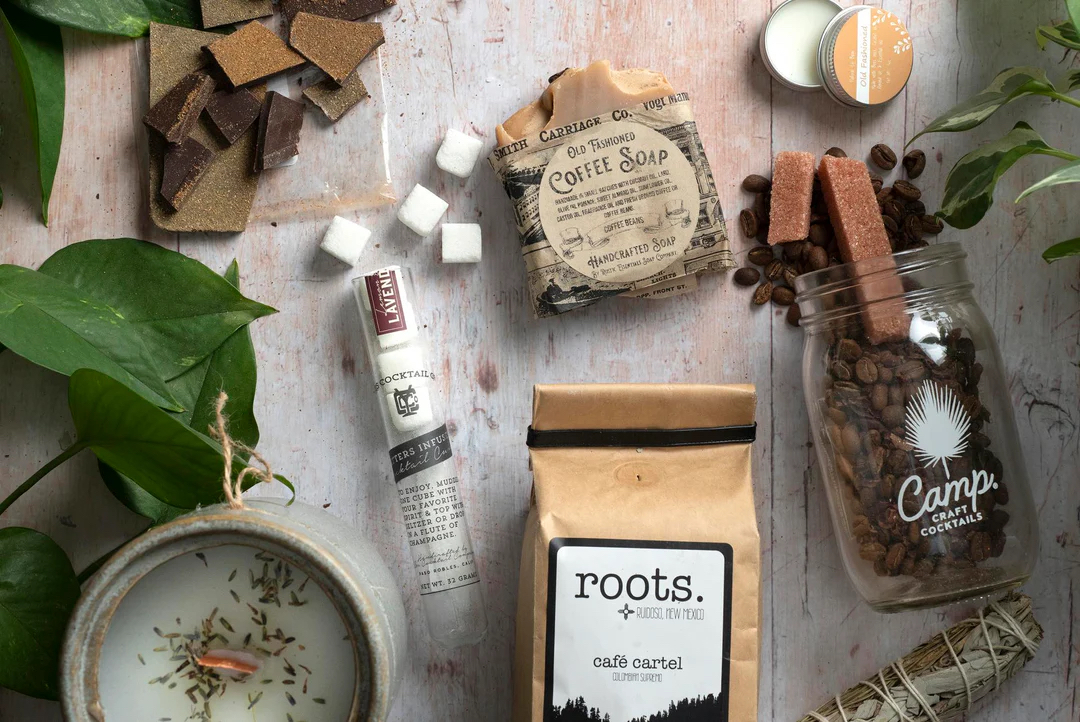 Flat lay of soap, coffee soap, coffee beans, sugar cubes, and a plant on a light surface.