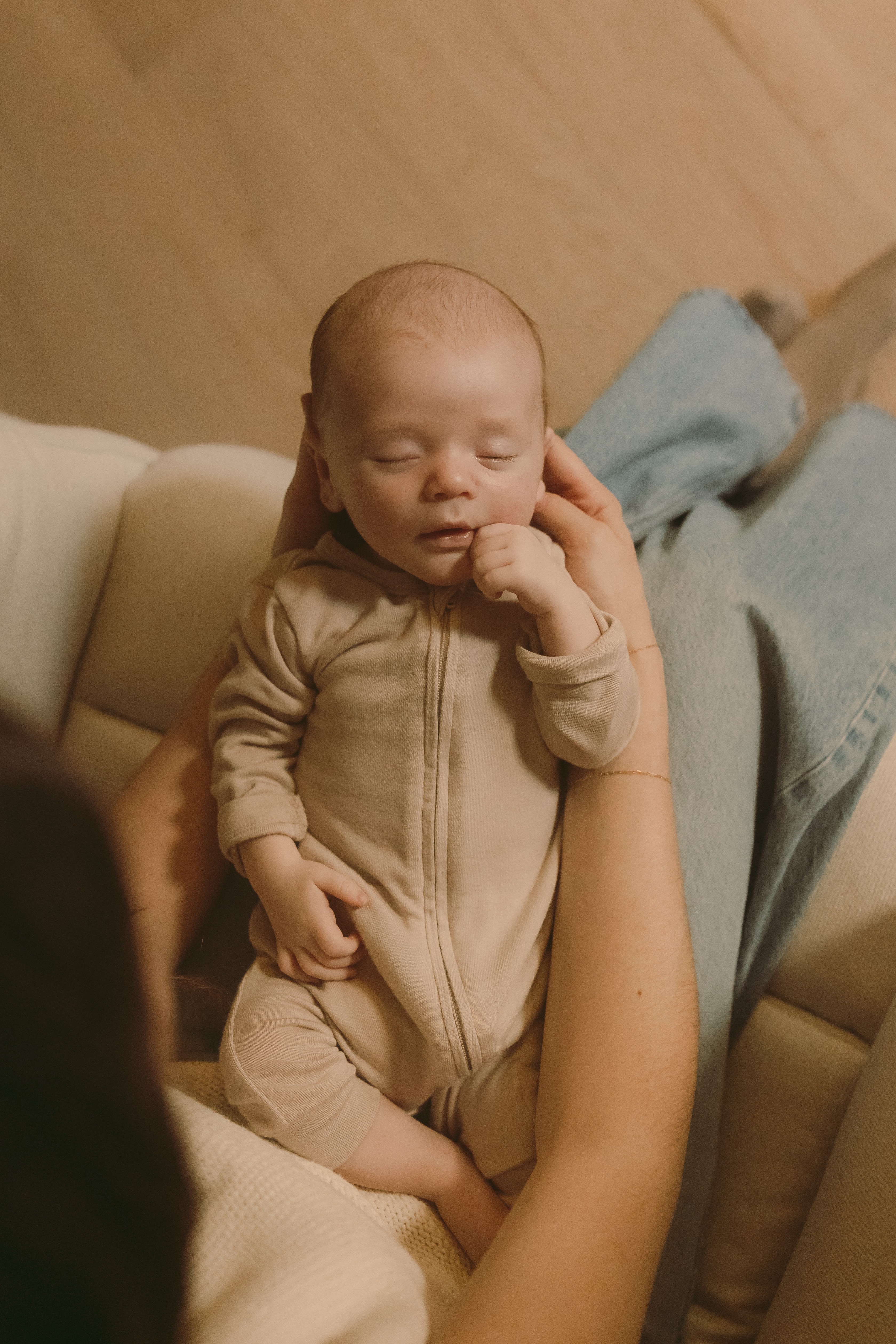 Baby with eyes closed, sitting on a person's lap, touching face, in a cozy indoor setting.