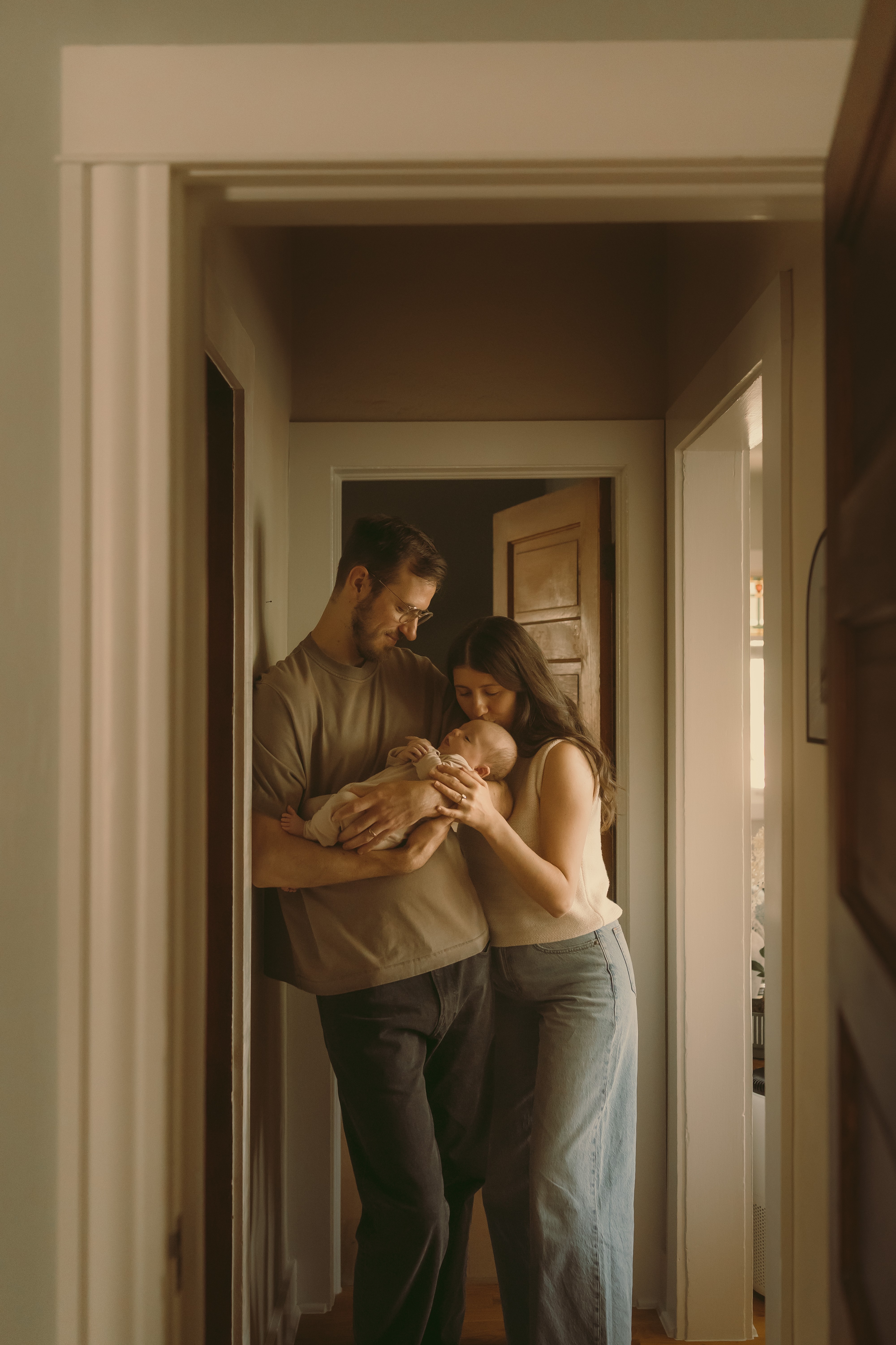 Two people holding a small dog in a doorway, with a wooden door and a window in the background.