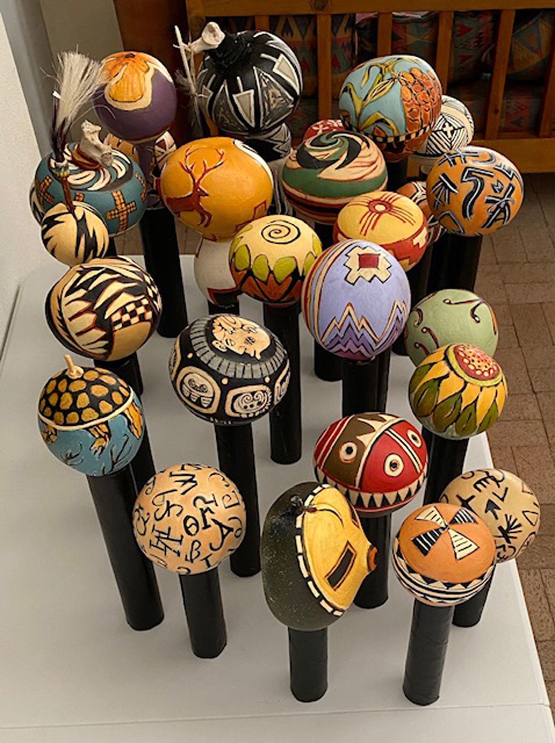 Colorful decorated eggs on black stands arranged on a table, with various patterns and designs, in a room with wooden furniture.