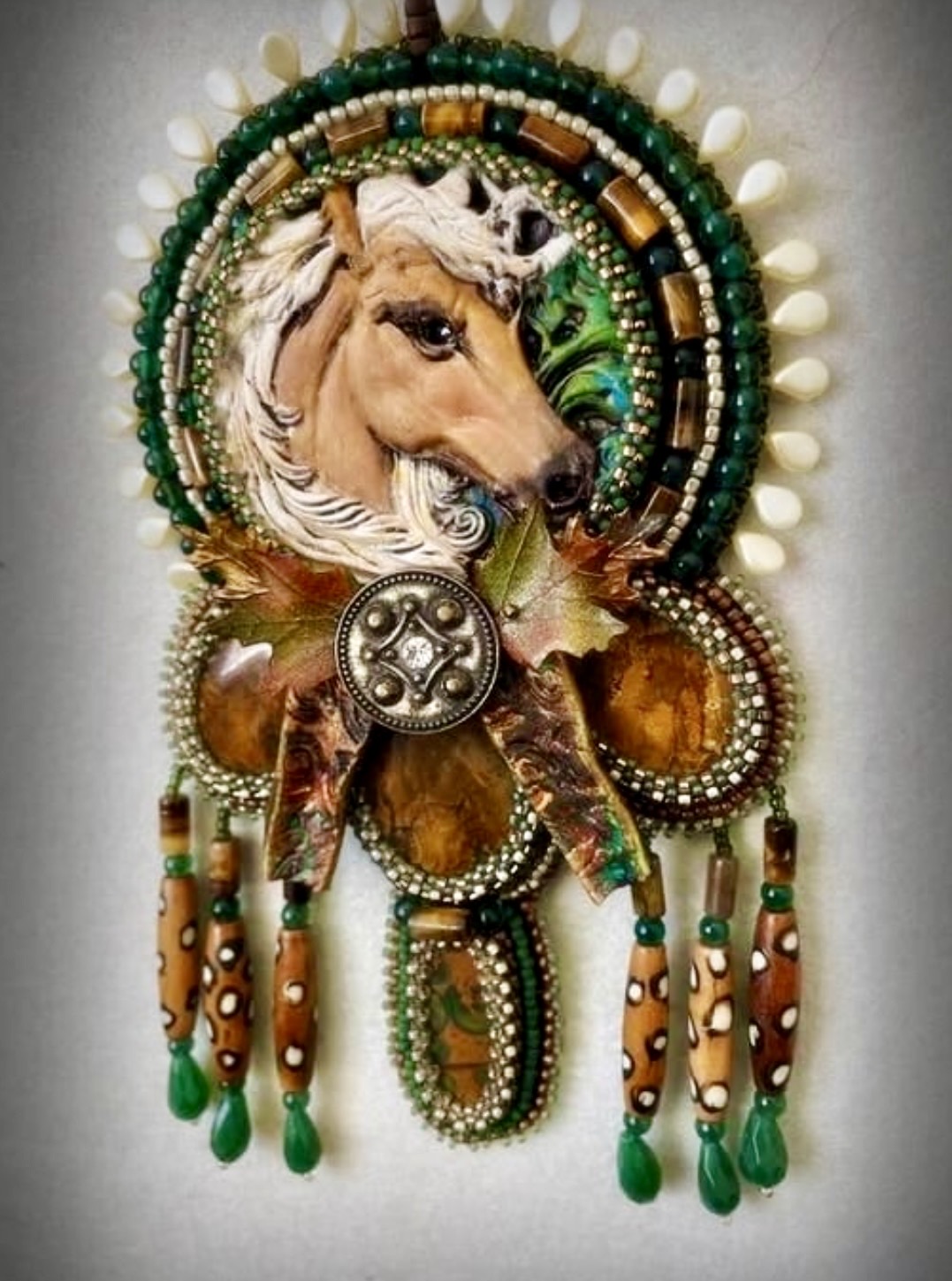 Decorative jewelry with a horse's face, beads, and hanging ornaments, featuring green, gold, and white colors.