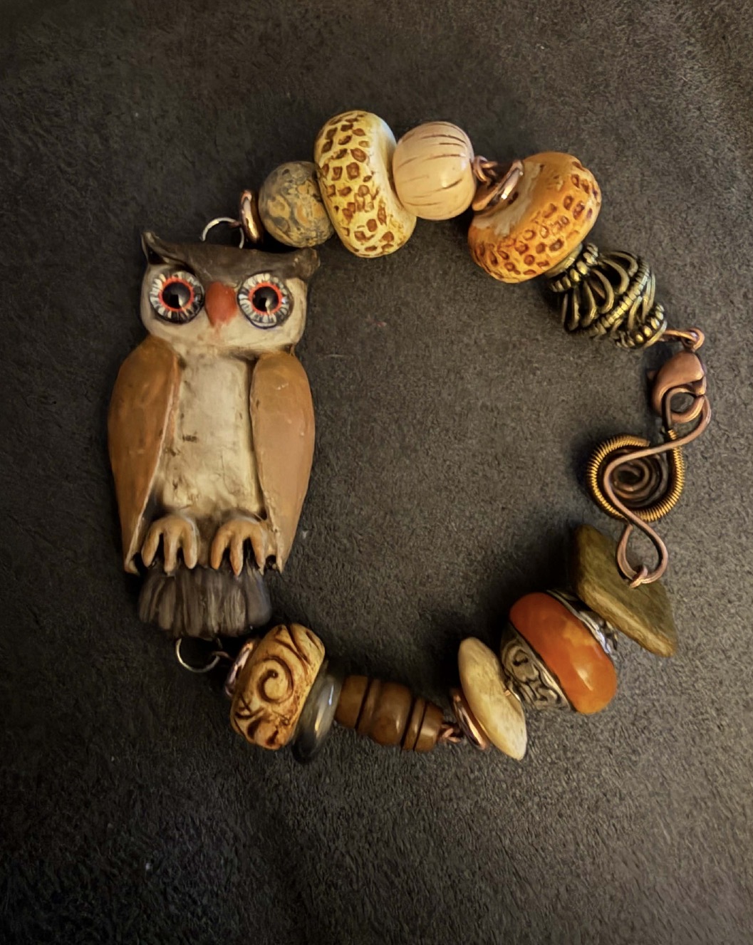 Bracelet with owl-shaped pendant and various colorful beads arranged in a circle on a dark surface.