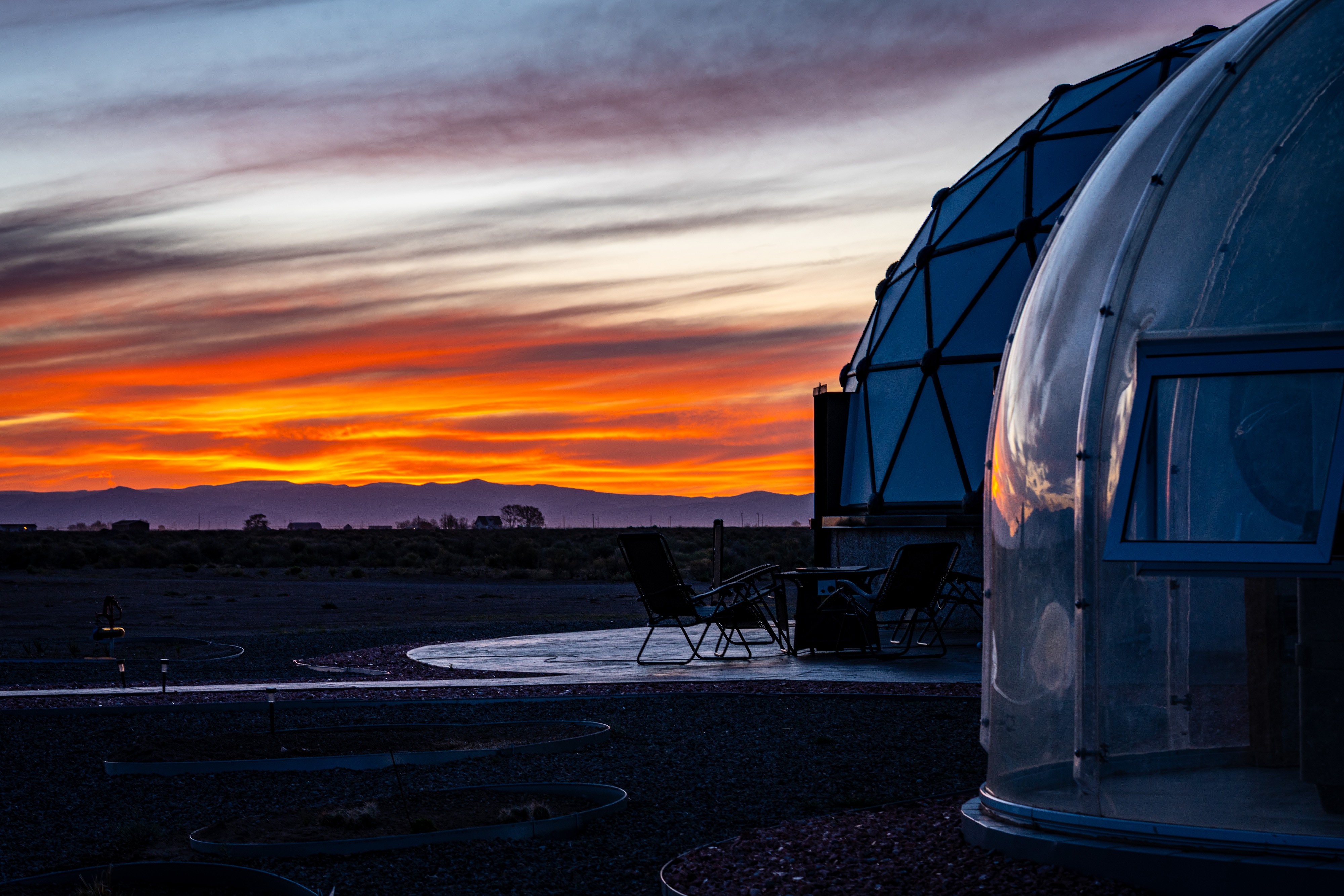 Dome-shaped observatory with chairs outside against a sunset sky with orange and purple clouds.