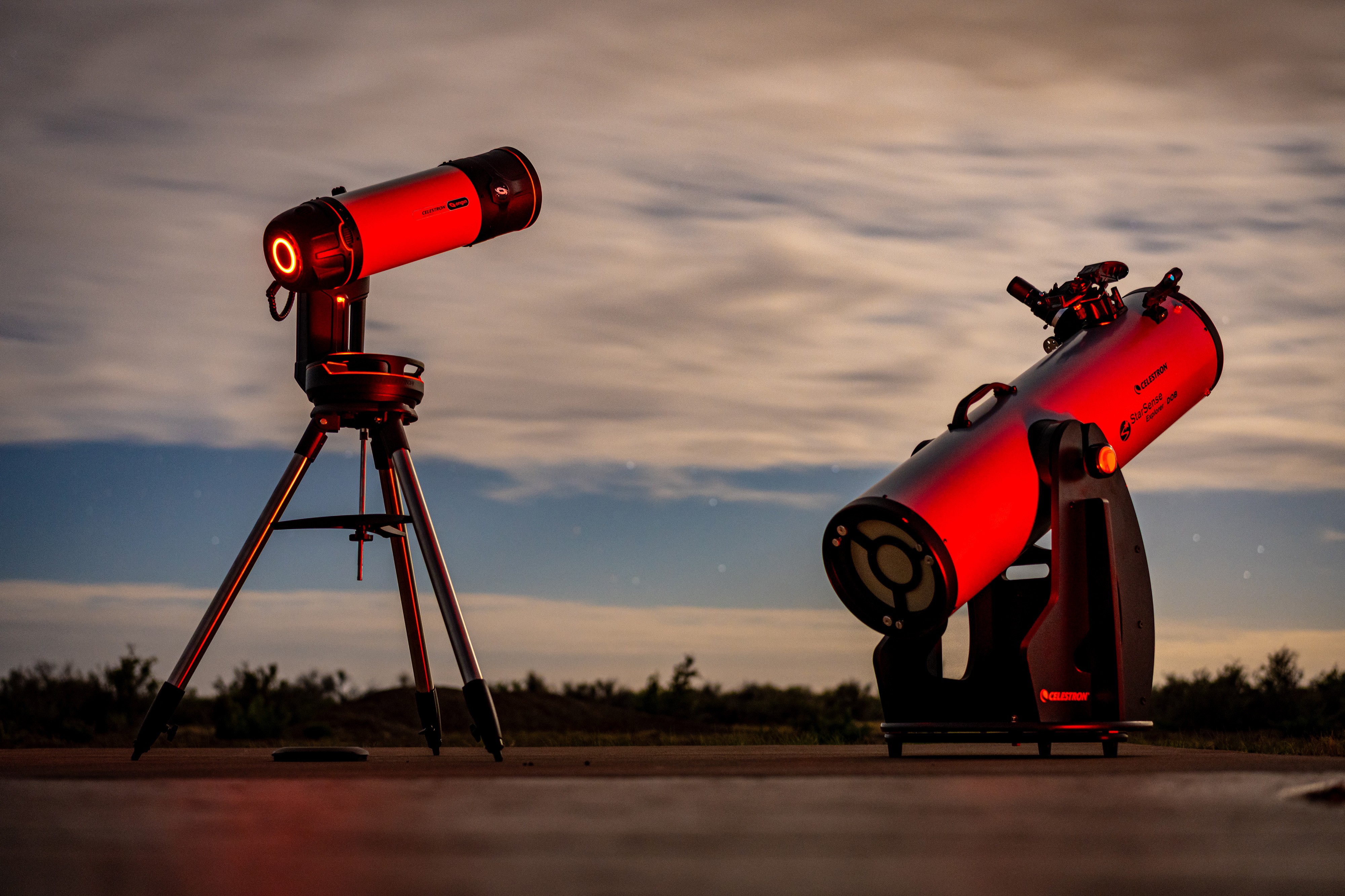 Two red telescopes outdoors on a flat surface with a cloudy sky background.