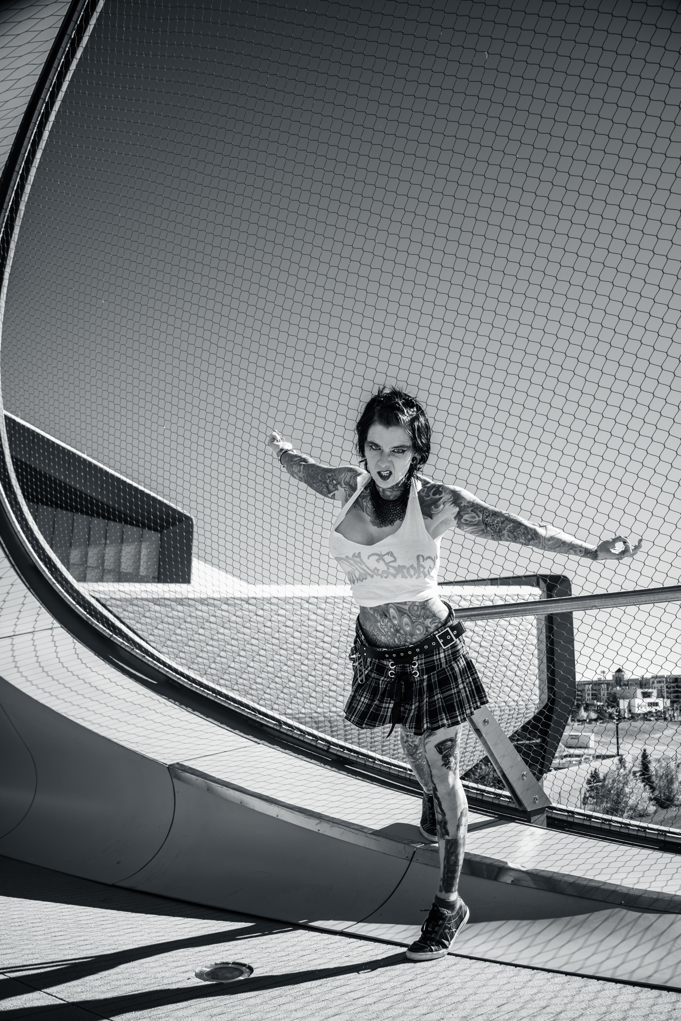 Young girl in a plaid skirt and crop top running on a curved outdoor structure with a railing, under a clear sky.