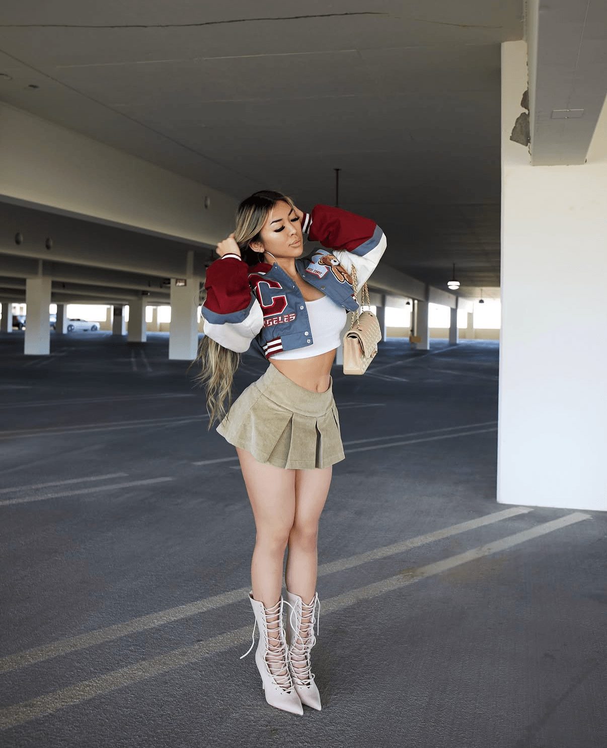 Young woman with long hair in a cropped jacket and beige skirt, standing in an empty parking garage, adjusting her hair.