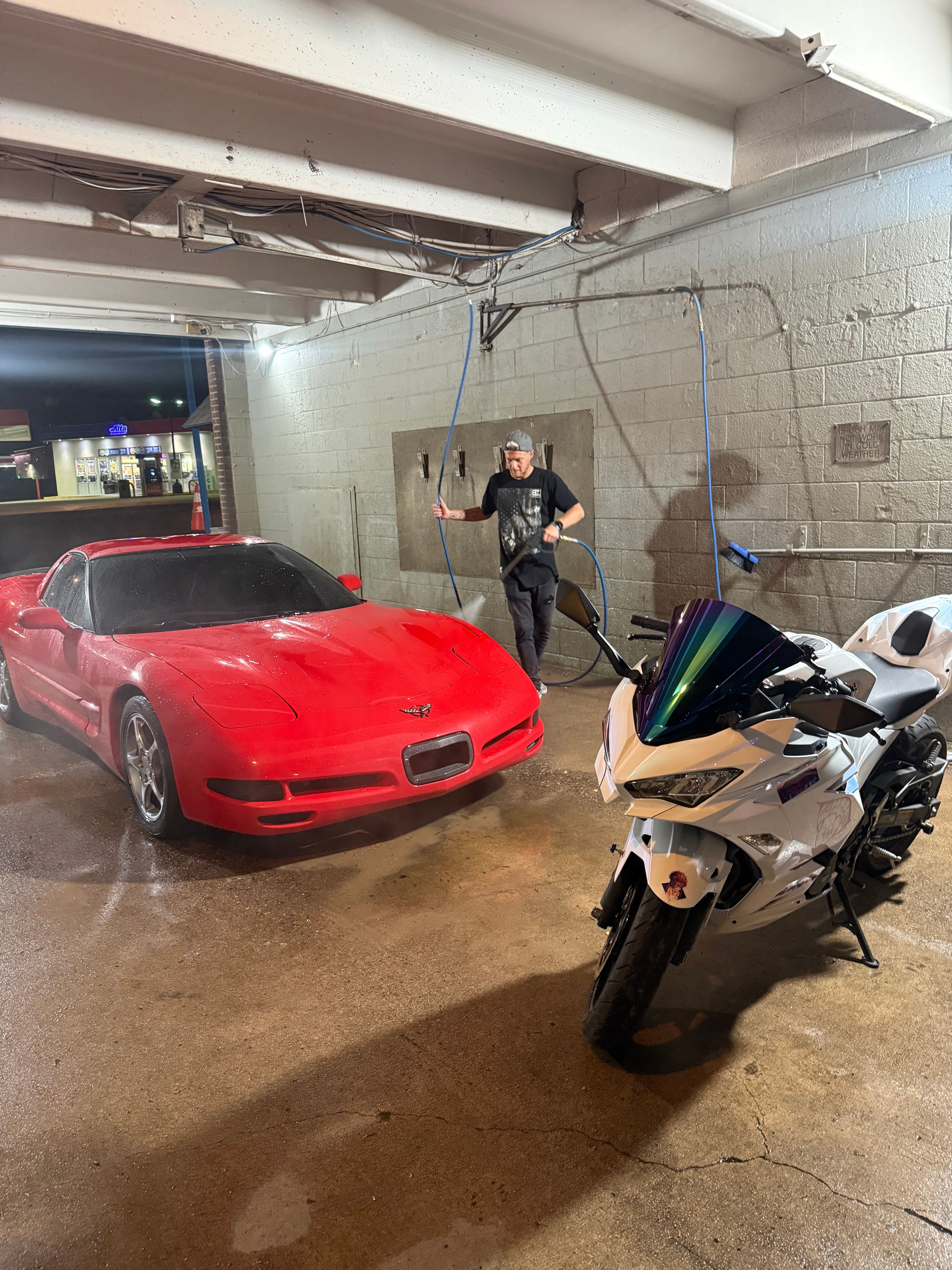 Person standing next to a red sports car in a garage with various equipment and tools around.