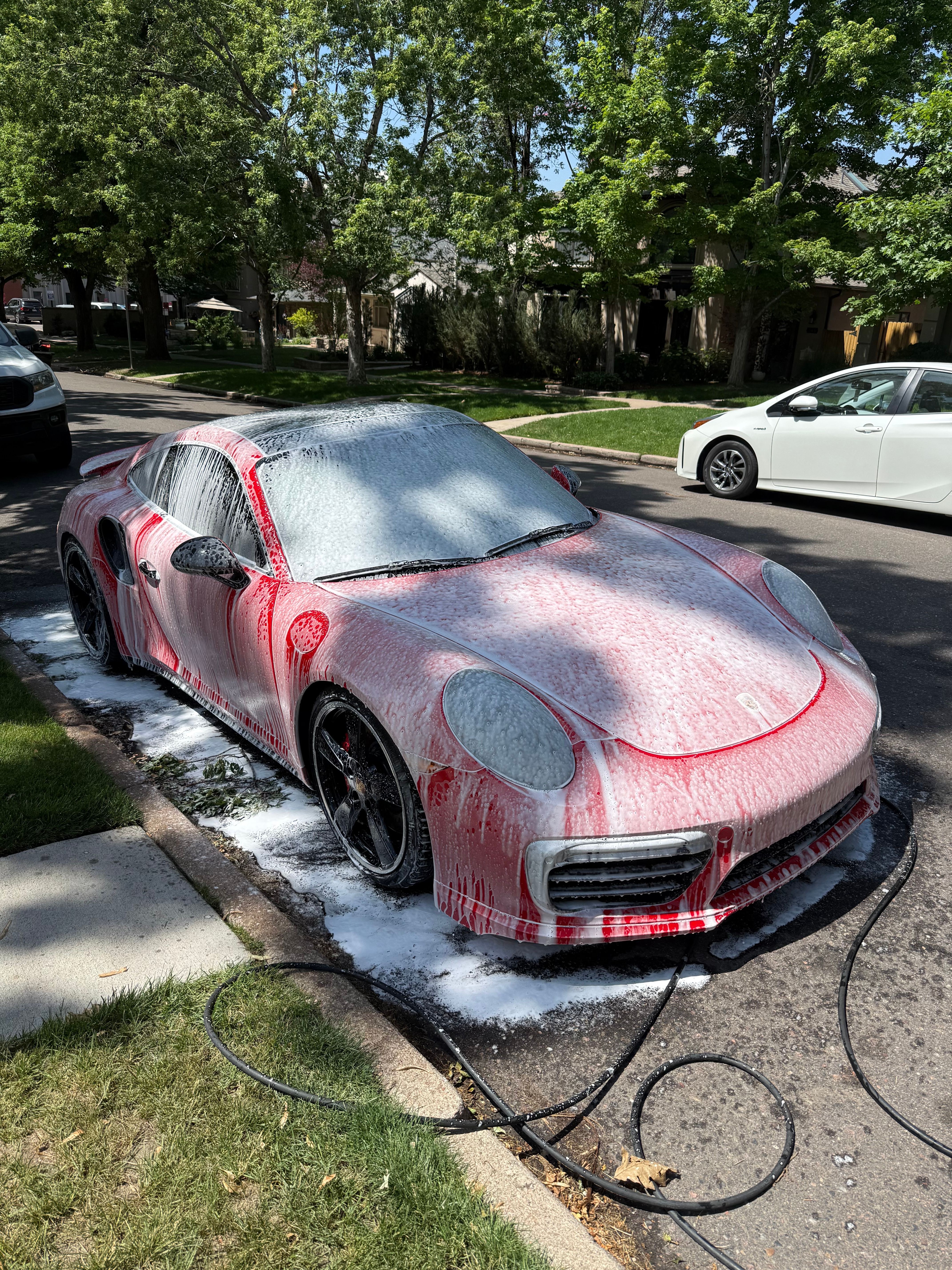Pink and black car parked on street with trees and other vehicles nearby.