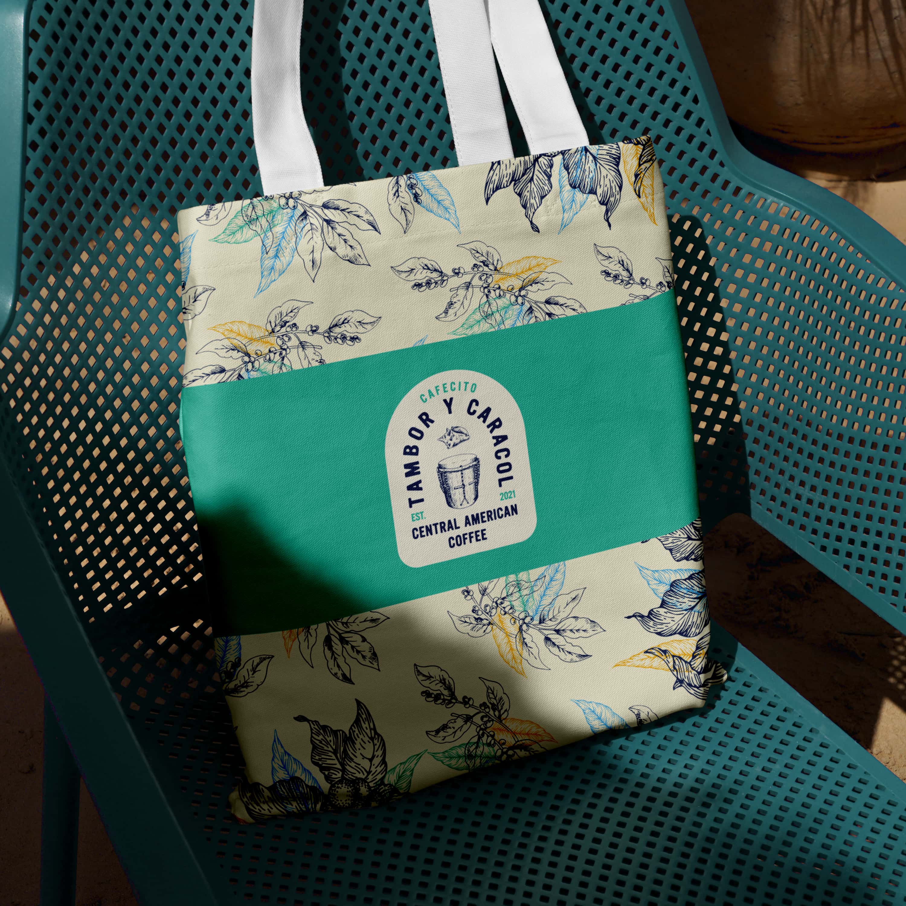 Tote bag with floral pattern and a logo for Timboboy Caracol coffee, resting on a teal chair.