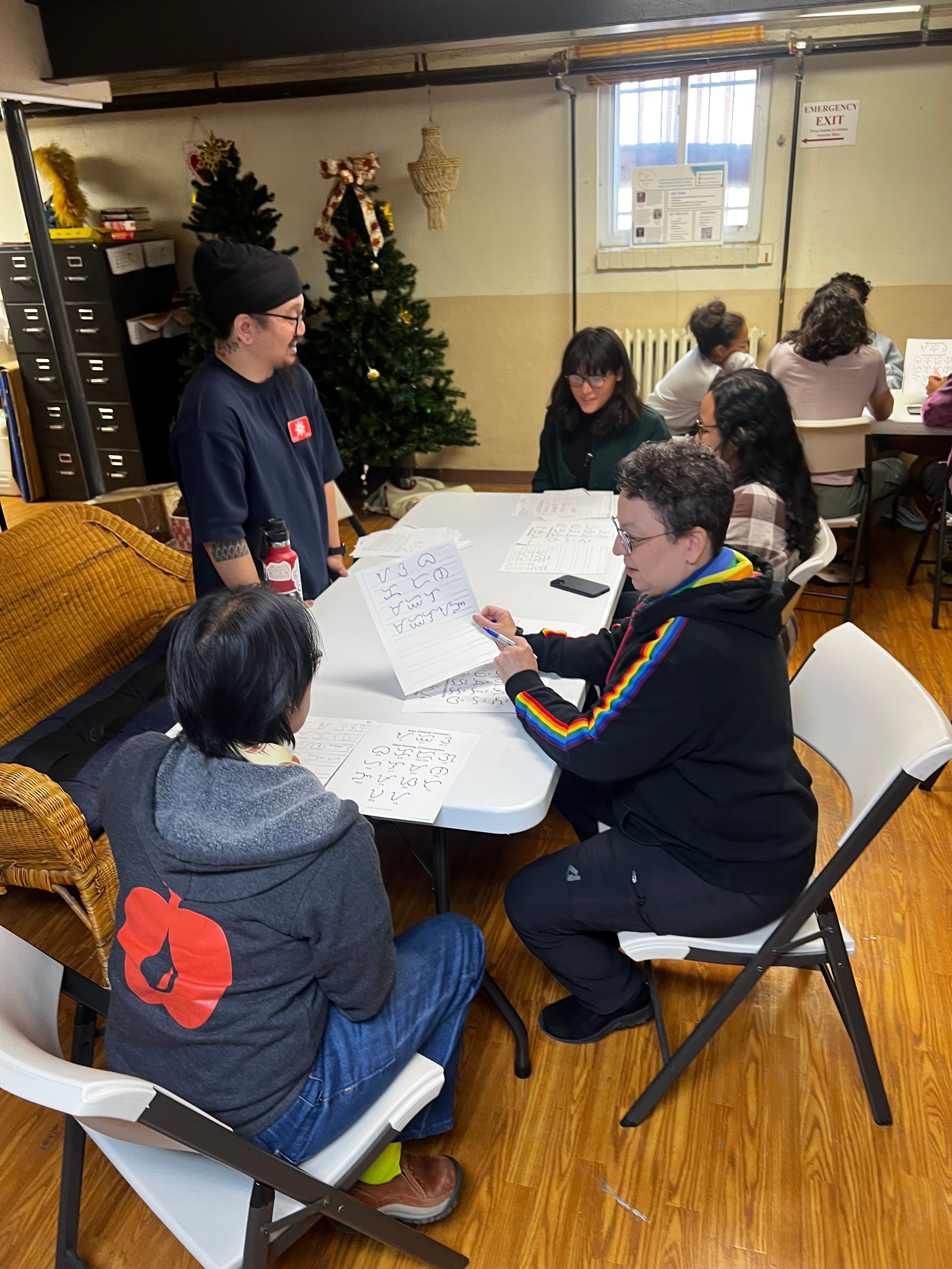 Group of people gathered around a table with papers, in a room with a Christmas tree and wooden floor.