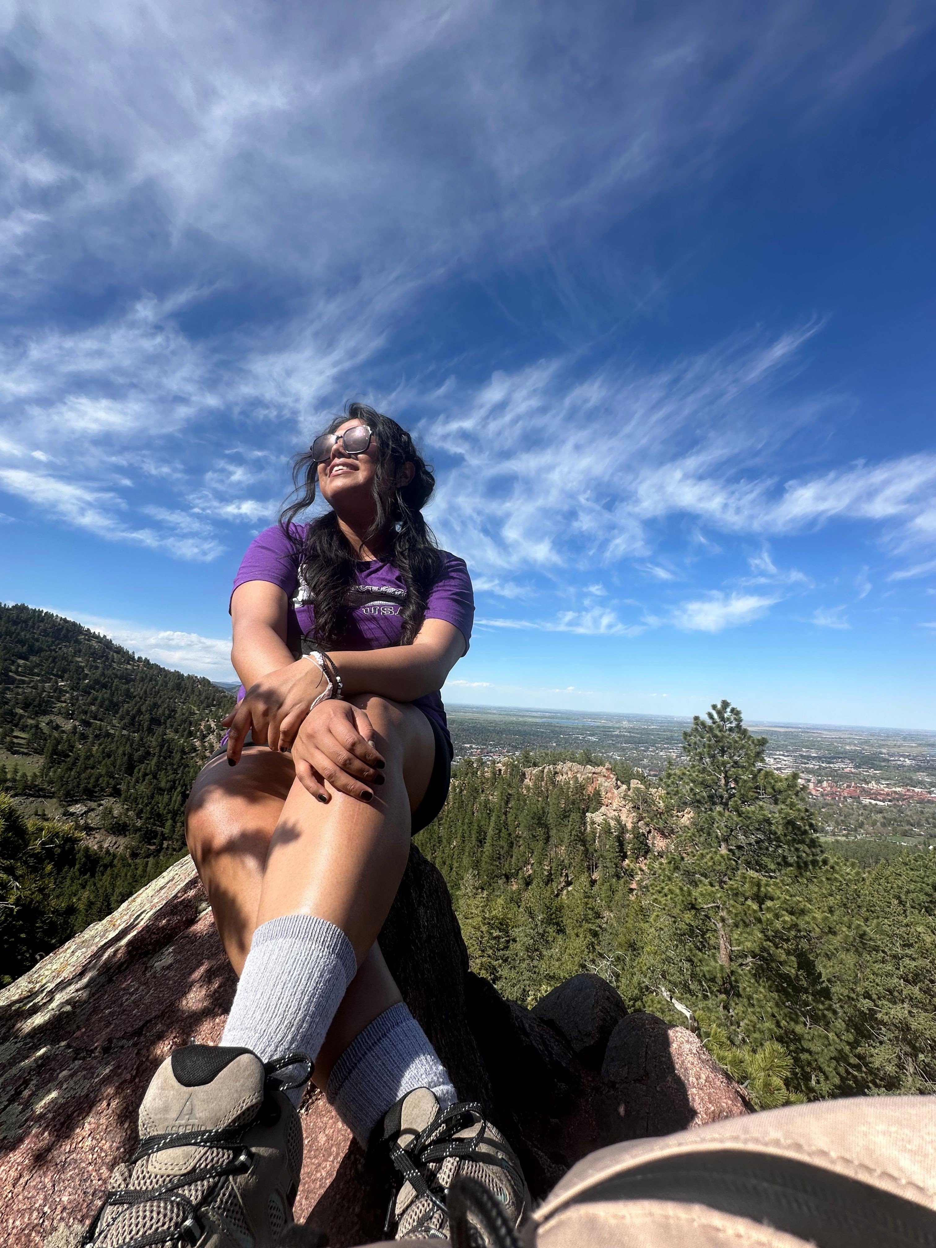 Person sitting on a rock with a scenic landscape and blue sky in the background.
