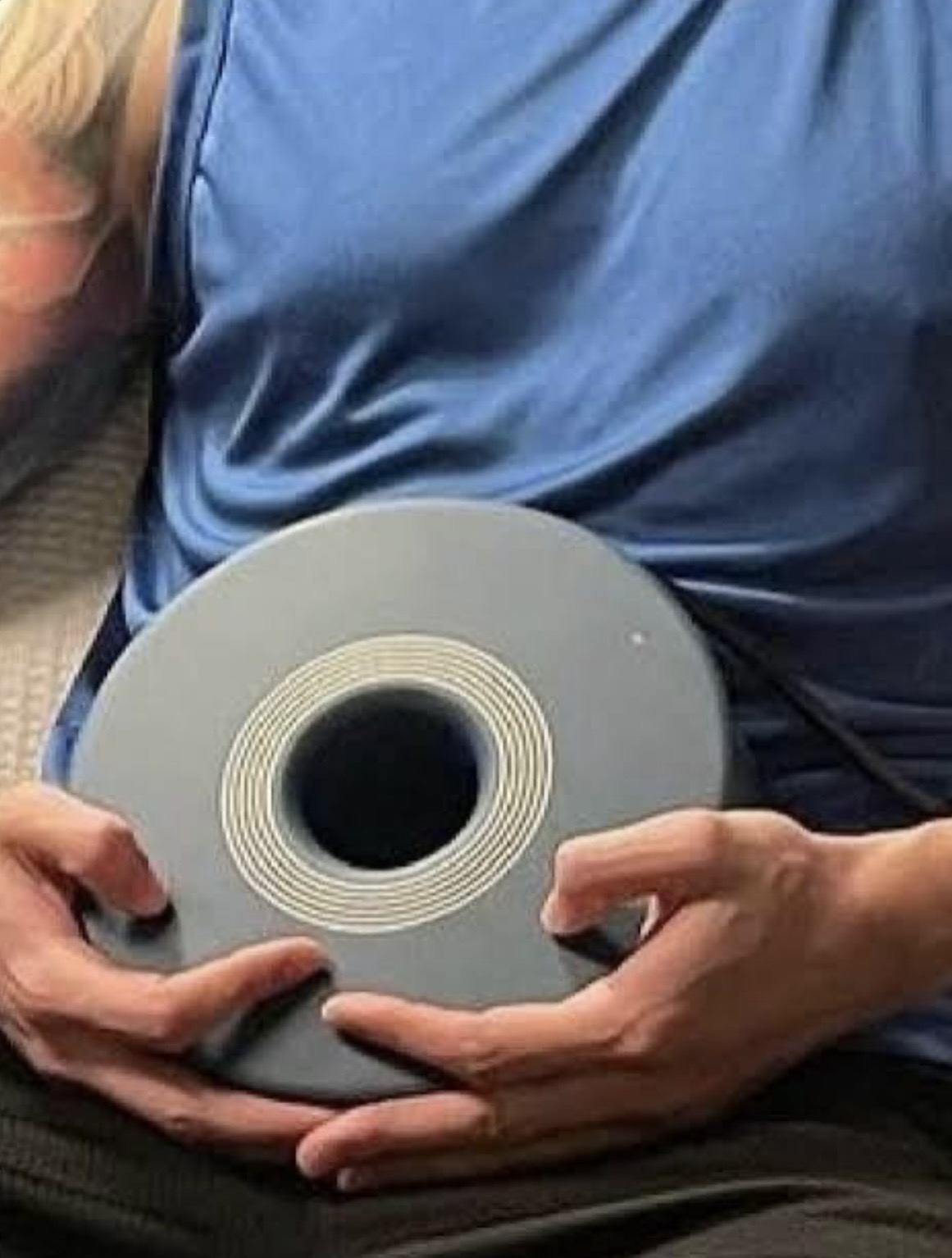 Person lying down holding a roll of tape or adhesive with both hands, wearing a blue shirt.