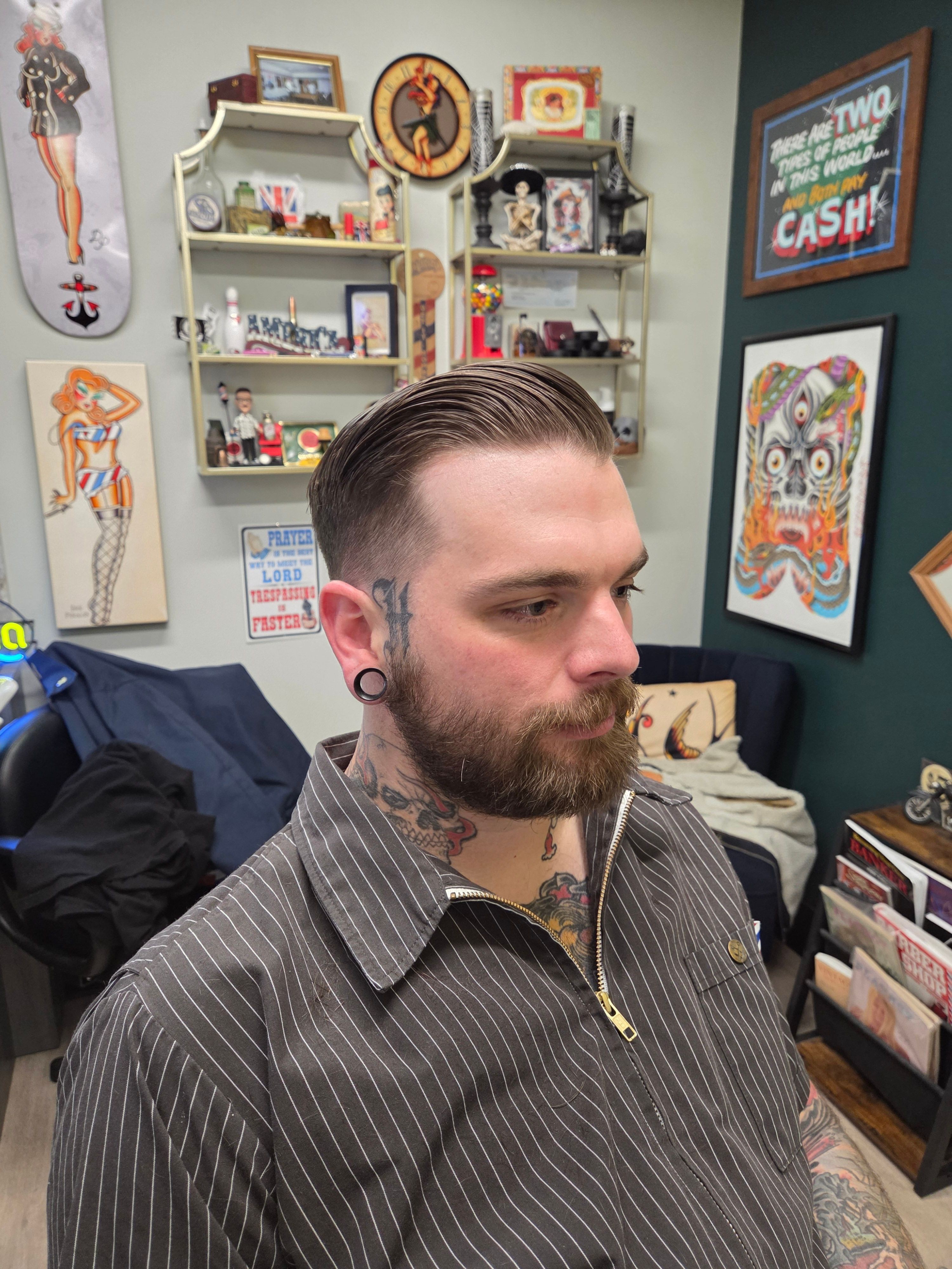 Side profile of a man with a beard and slicked-back hair, wearing a pinstripe shirt, in a room with artwork and shelves.