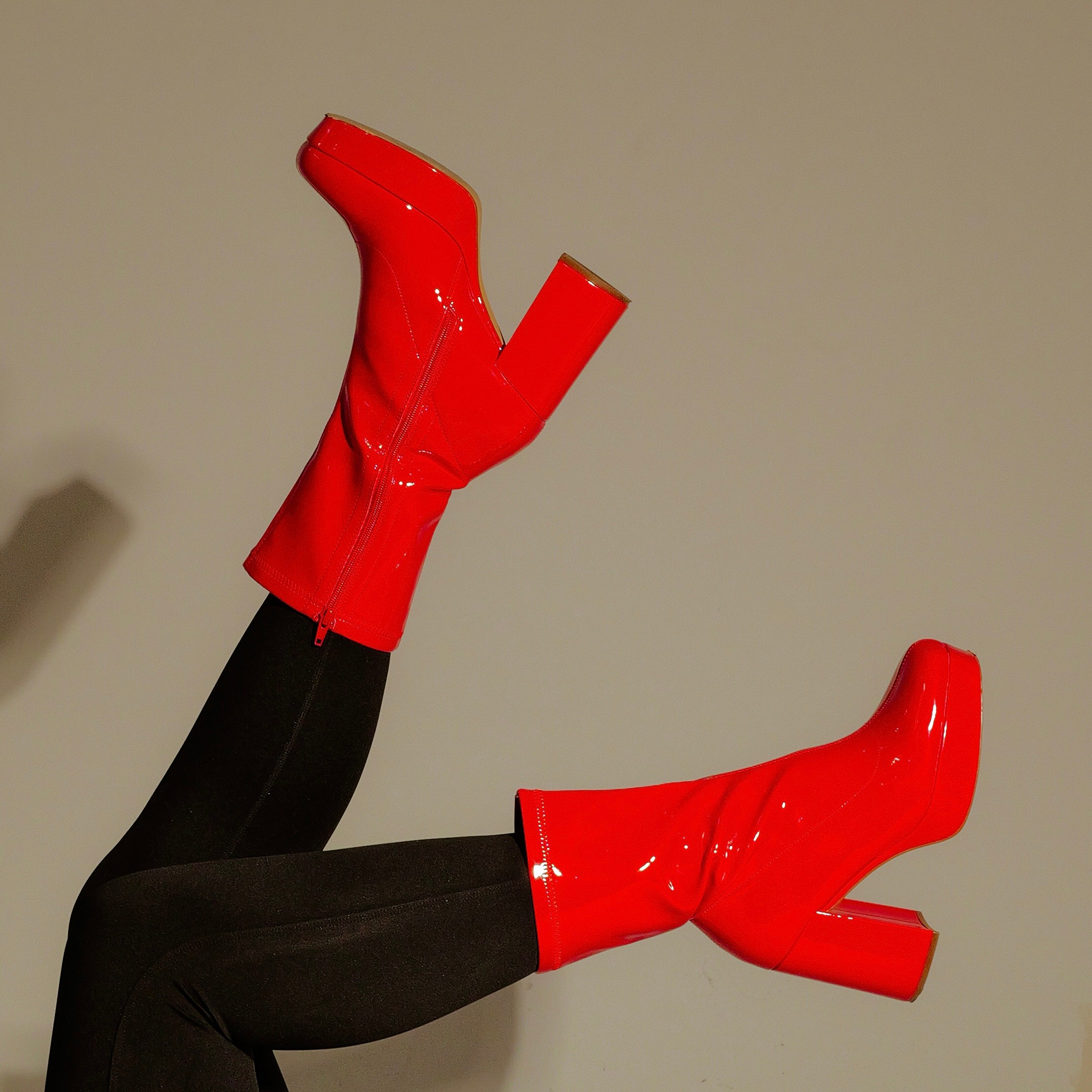 Person wearing red high-heeled boots and black leggings with legs raised against a plain background.