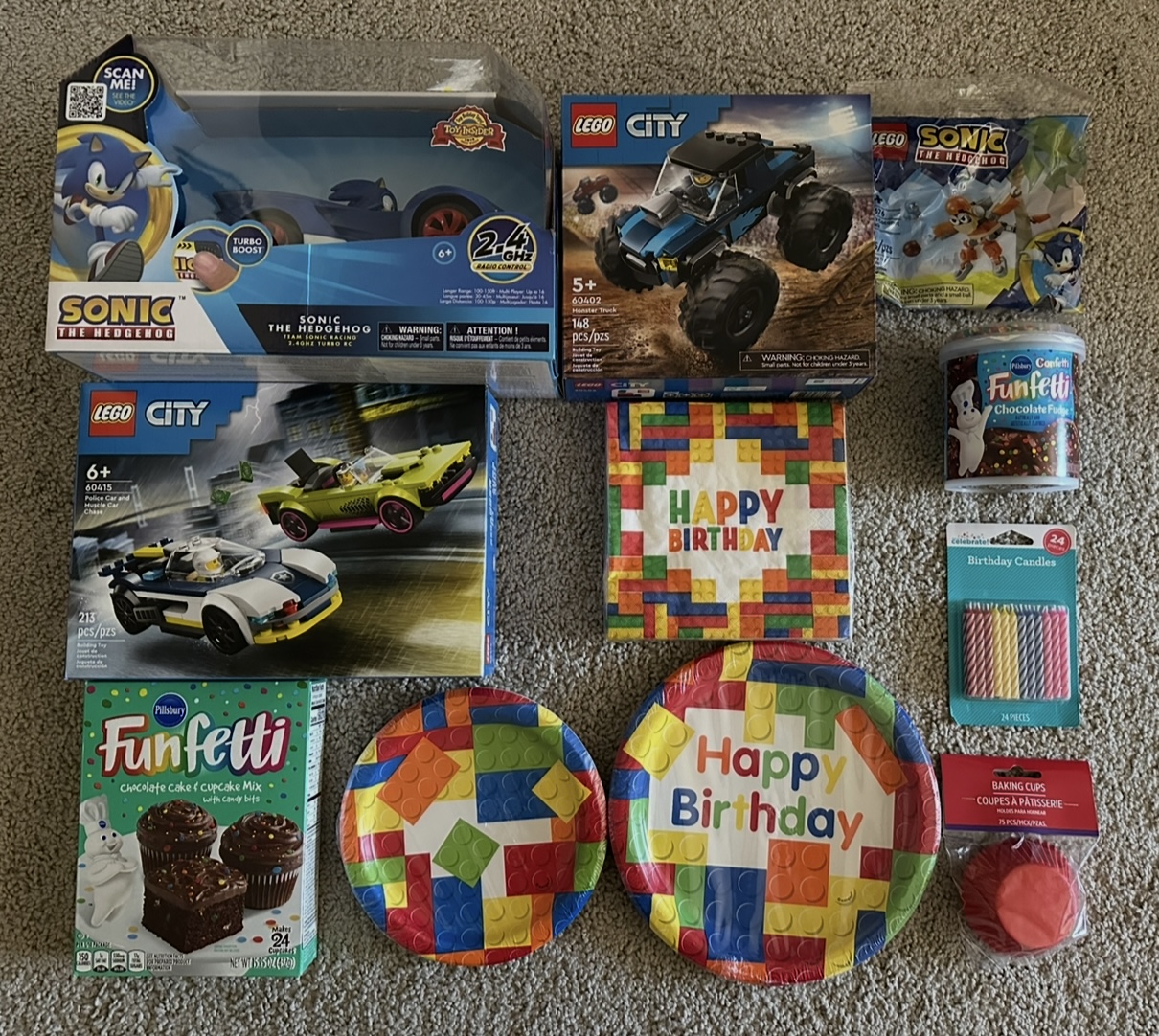Collection of LEGO sets, birthday plates, party hats, and snacks on carpet, celebrating a birthday.