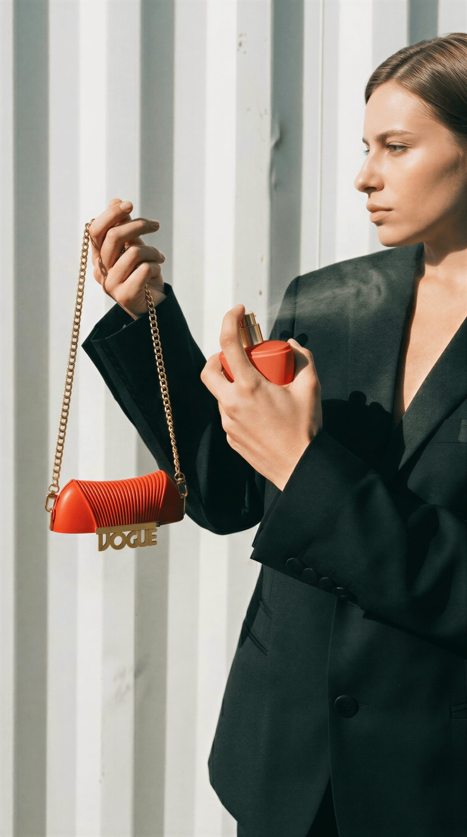 Woman in black blazer holding a small orange purse and a compact mirror, standing near vertical white panels.