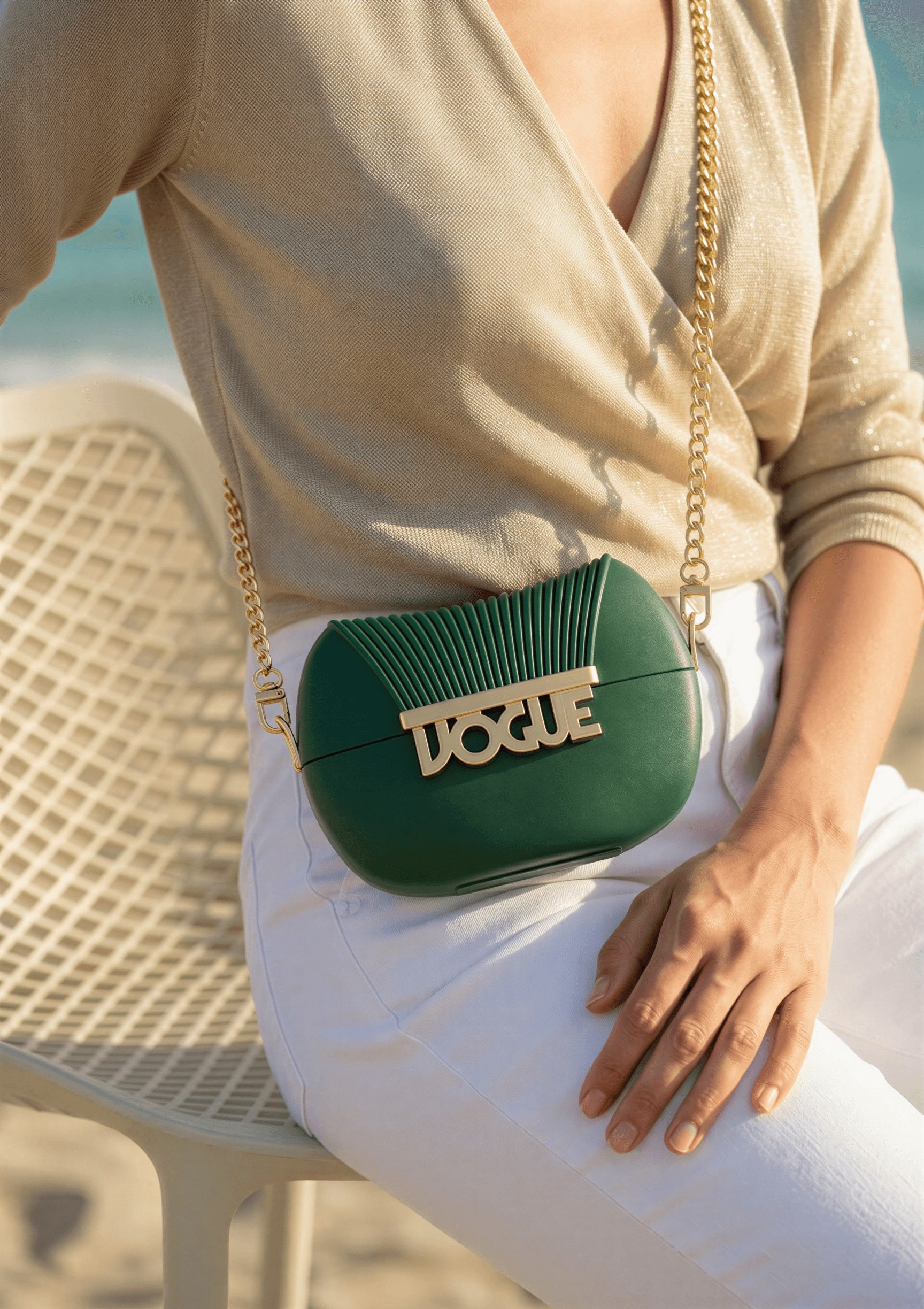 Person sitting outdoors with a green handbag featuring a gold chain and logo, wearing a beige top and white pants.