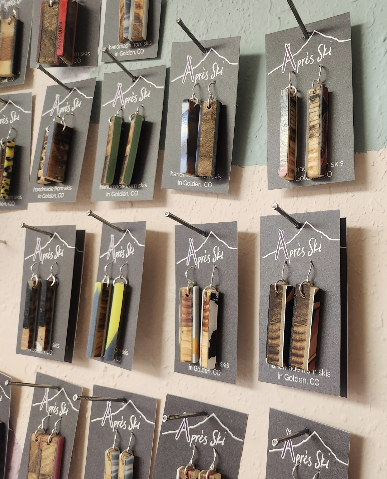 Display of earrings hanging on cards on a wall, arranged in rows with various colors and patterns.