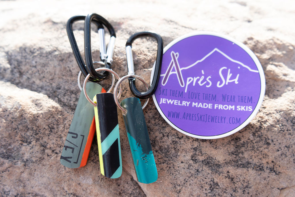 Keychain with multiple tags and a purple circular sticker on a sandy surface.