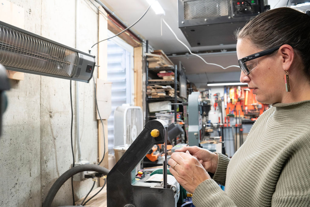Woman working with tools in a workshop, shelves with equipment in background.