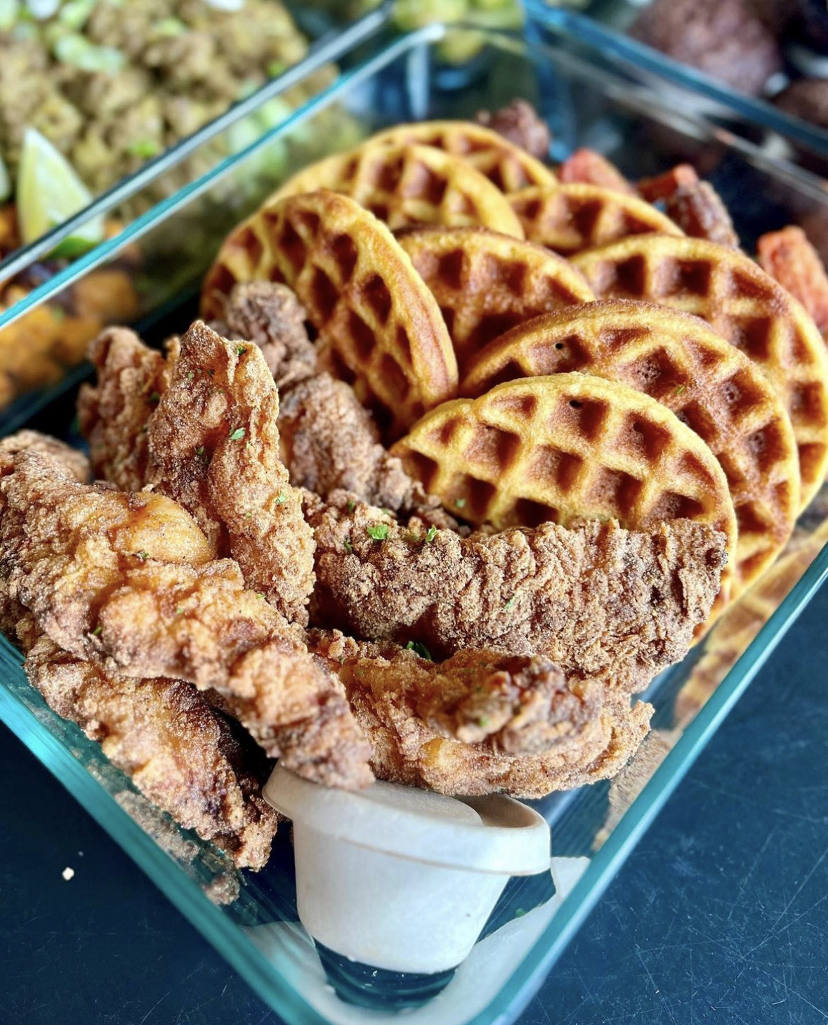 Fried chicken pieces, waffle fries, and a small container of dipping sauce in a glass dish.