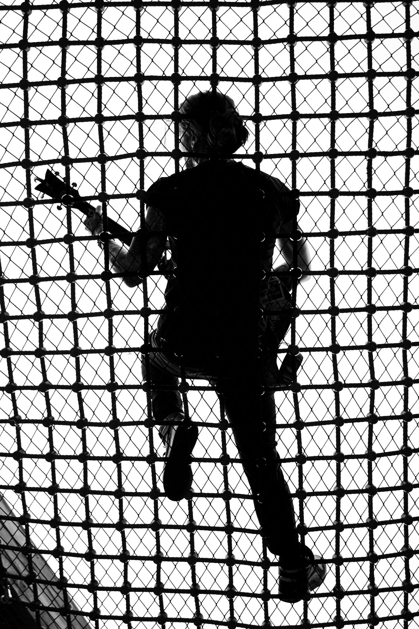 Silhouette of a person lying on a grid surface, with one arm raised, against a bright background.