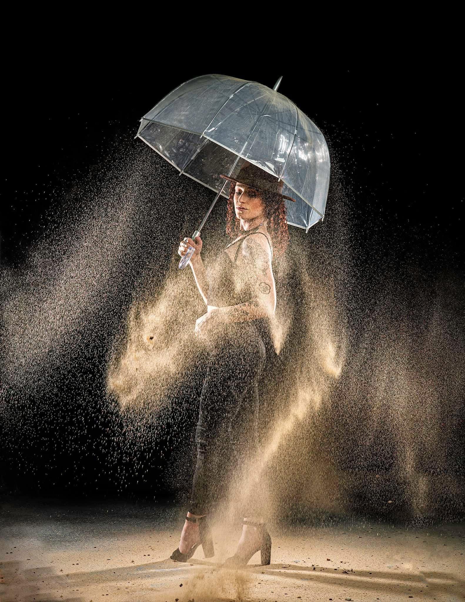 Woman holding a transparent umbrella in the rain, surrounded by splashing water, wearing a dress and high heels.