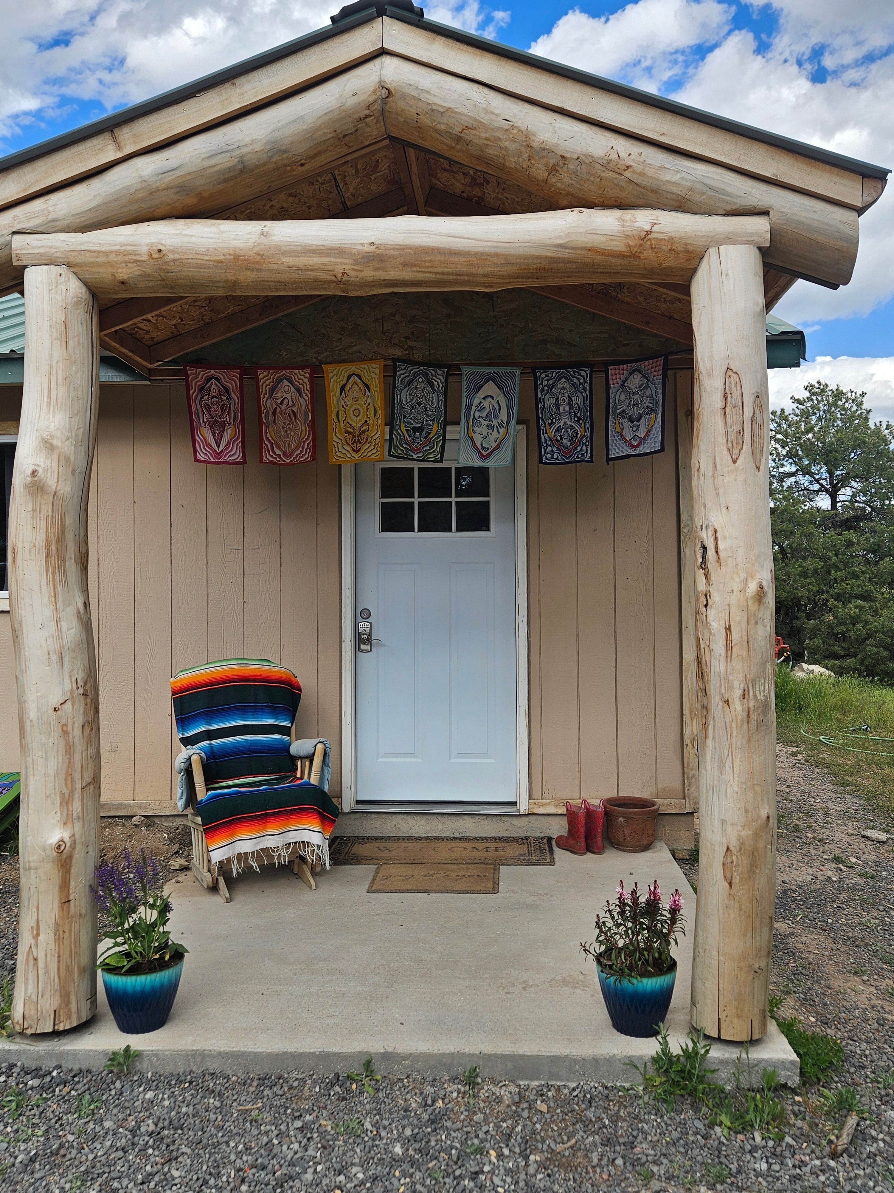 Small wooden structure with a door, decorated with framed pictures, and colorful blankets on a bench outside.