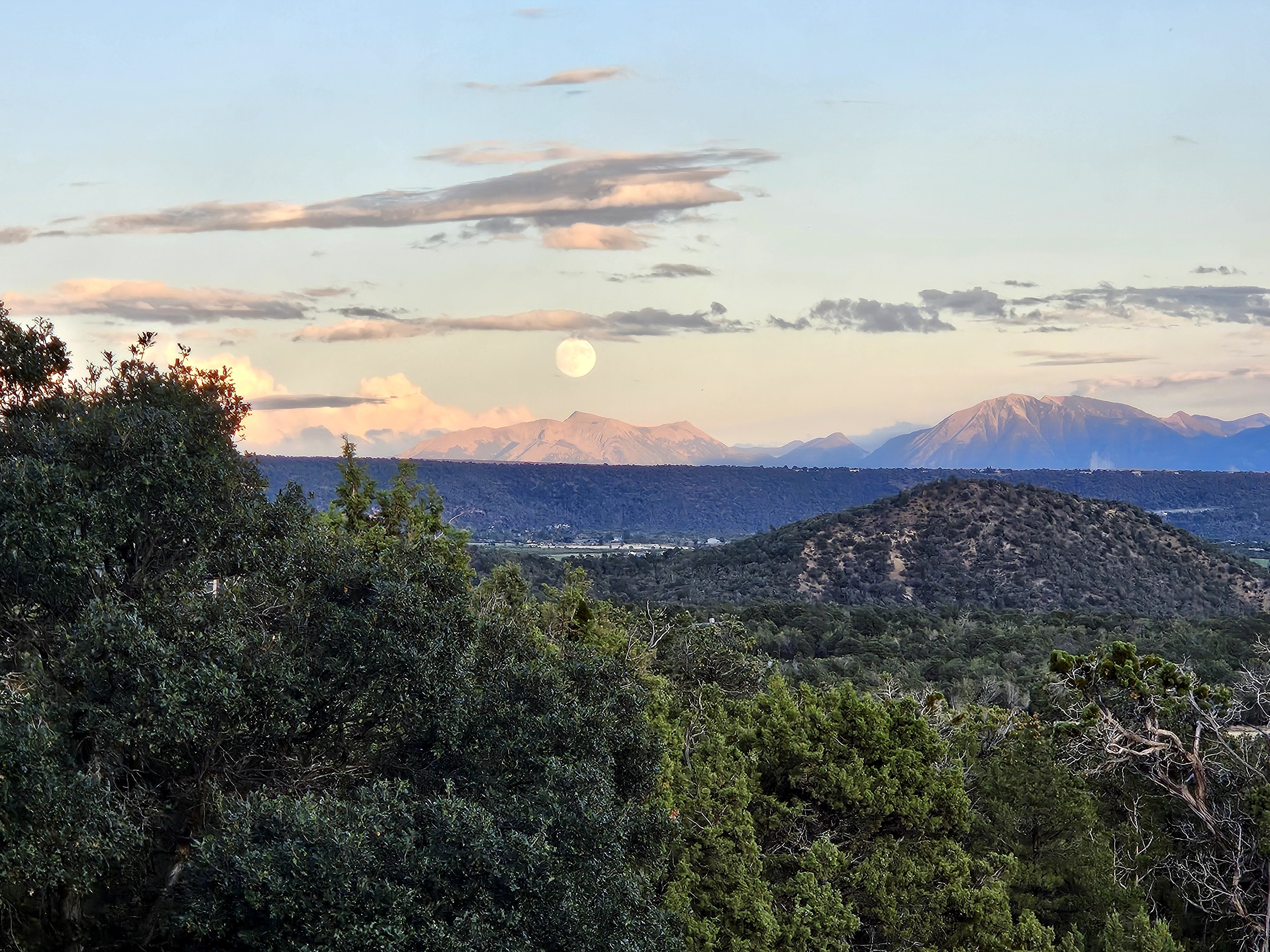 Landscape with trees, hills, mountains in the distance, and a full moon in the sky.