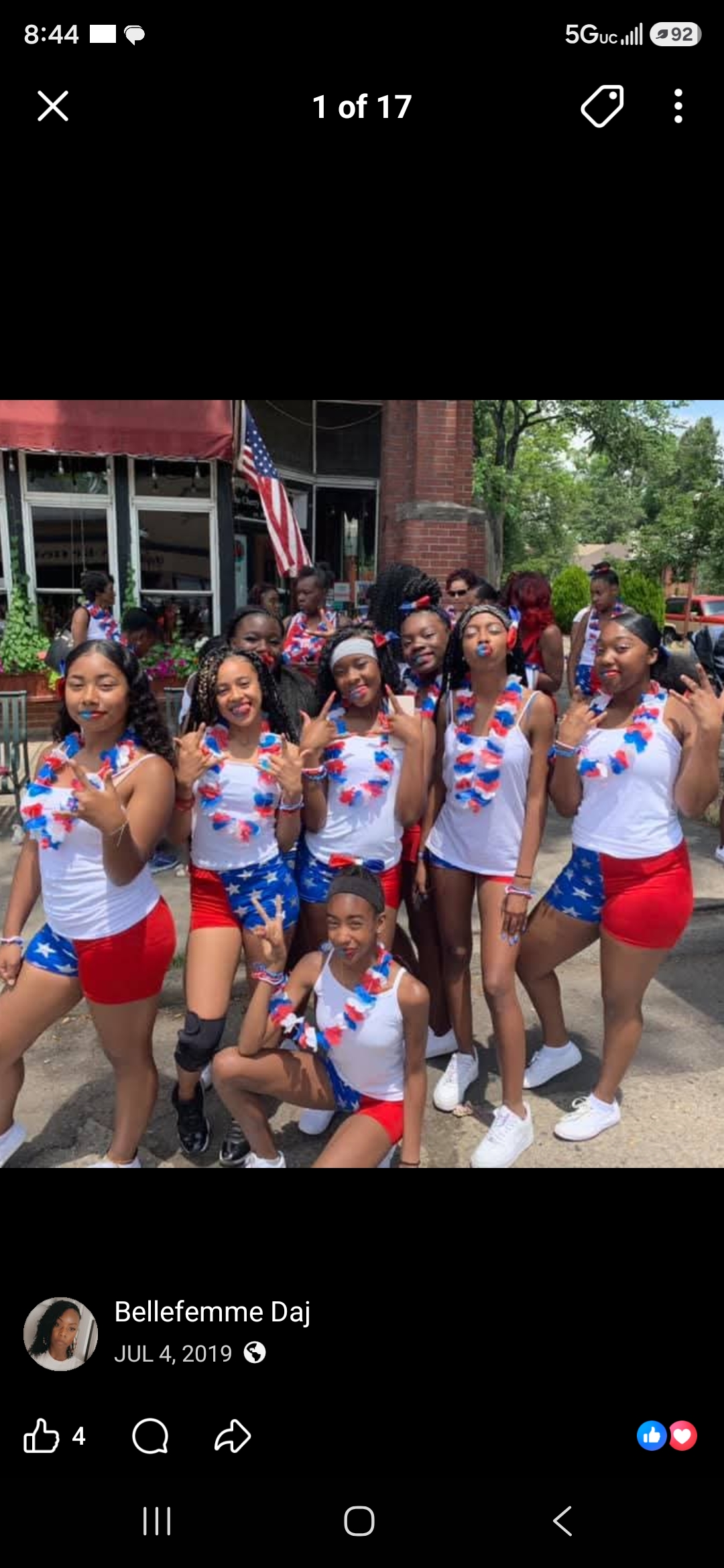 Group of children in patriotic outfits posing outdoors with trees and a building in background.