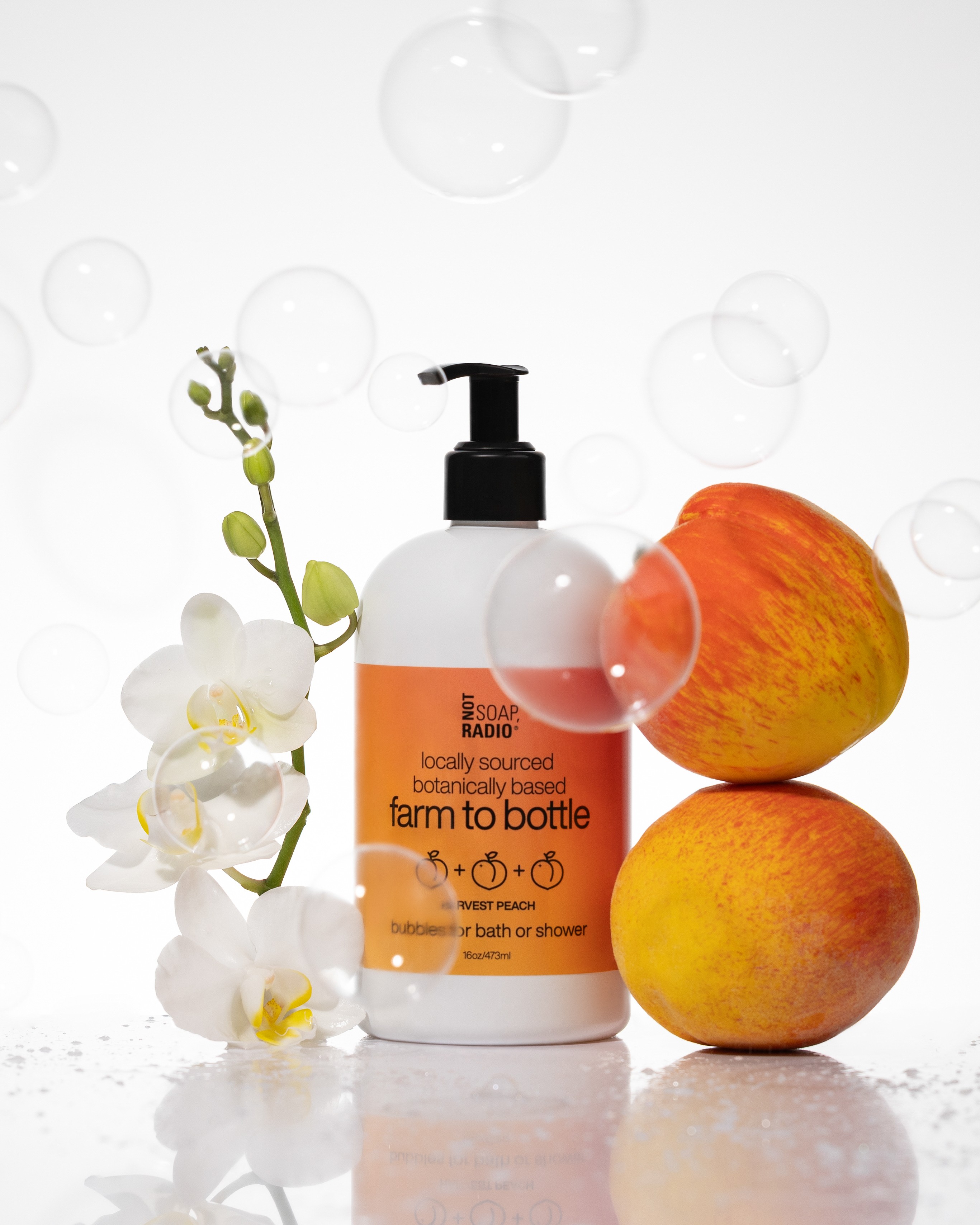 Pump bottle with orange and yellow peaches, white flowers, and bubbles on a reflective surface.