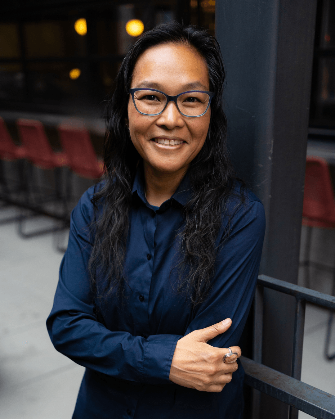 Woman with glasses smiling, wearing a dark blue shirt, standing outdoors at night.
