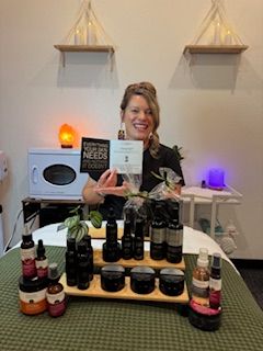 Woman smiling behind a table with various bottles, holding a certificate, in a room with shelves and decorative lights