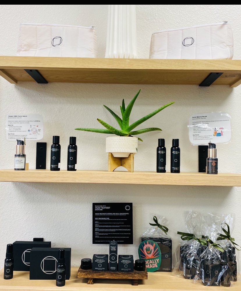 Shelves with skincare products, a potted plant, and a black sign, with a white wall background.