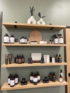 Three wooden shelves with skincare and cosmetic products, and two white vases with small plants on top, against a green wall.