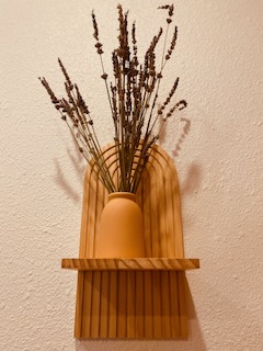 Vase with dried lavender flowers on a wooden wall-mounted shelf against a beige wall.