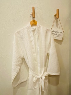 White bathrobe hanging on a hook, with a small sign hanging nearby on a wall, plain background.