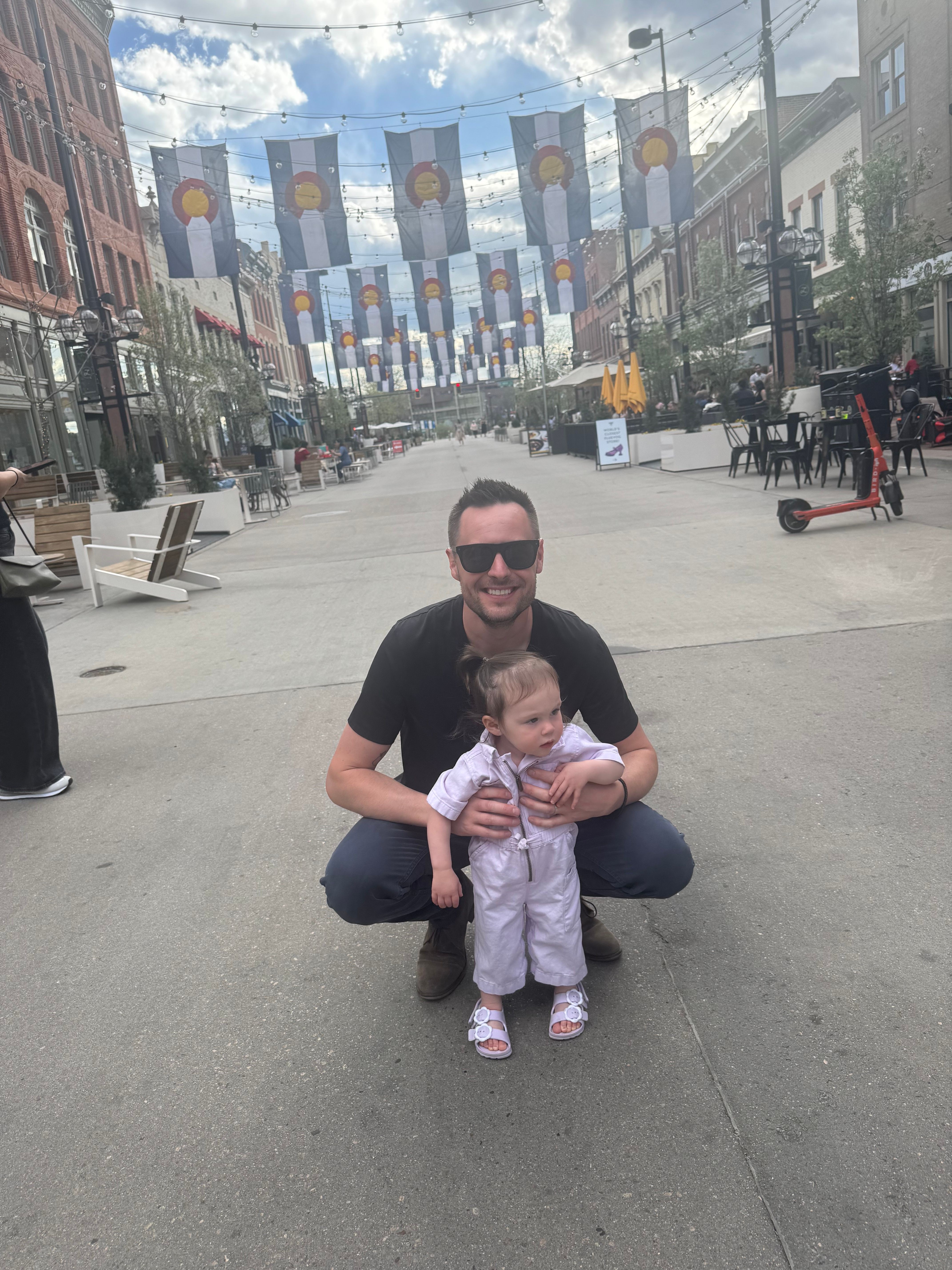 Person crouching on sidewalk holding a child, city street background with buildings and street signs.