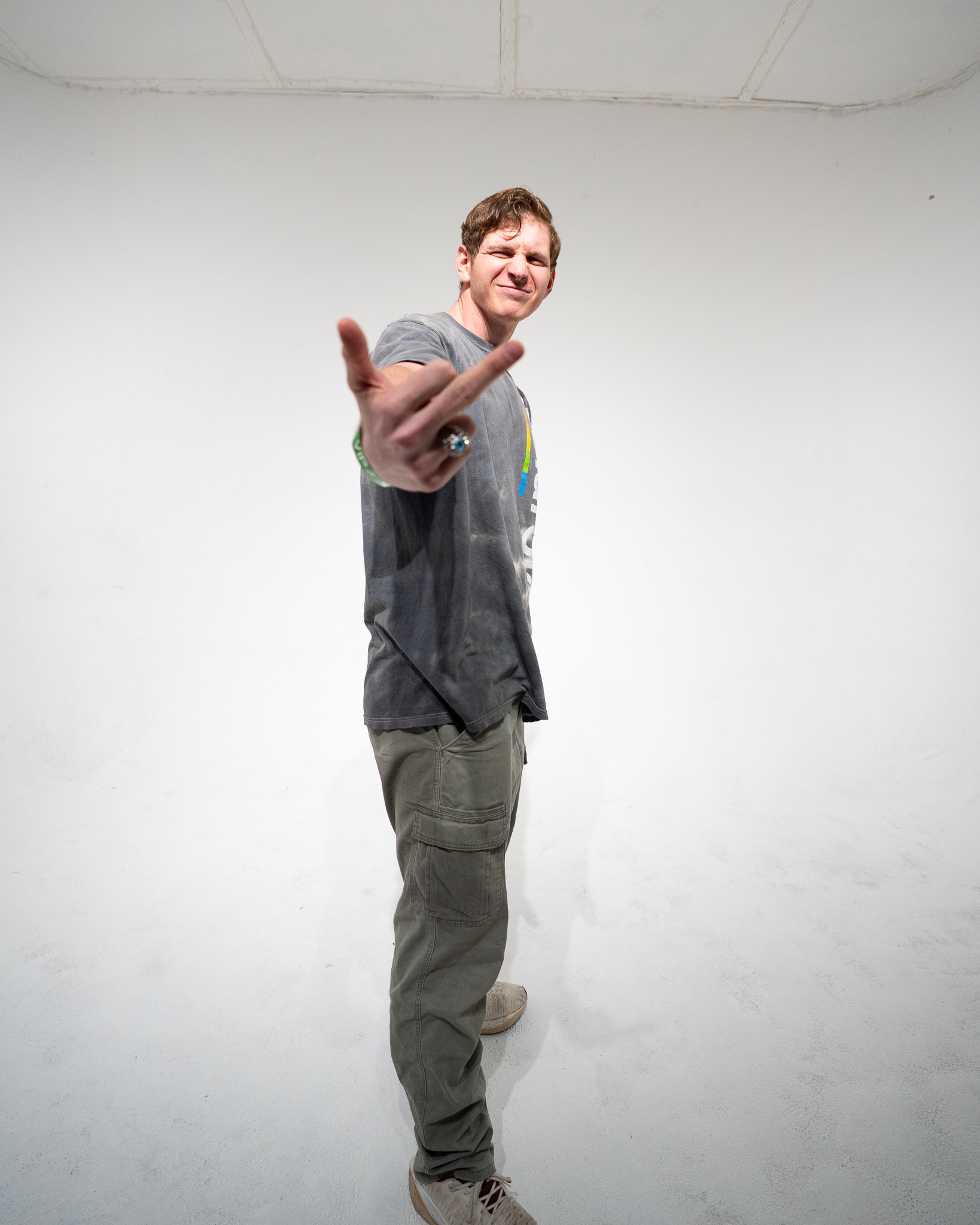 Young man smiling and extending his hand toward the camera in a white studio, casual clothing, standing with one foot slightly forward.