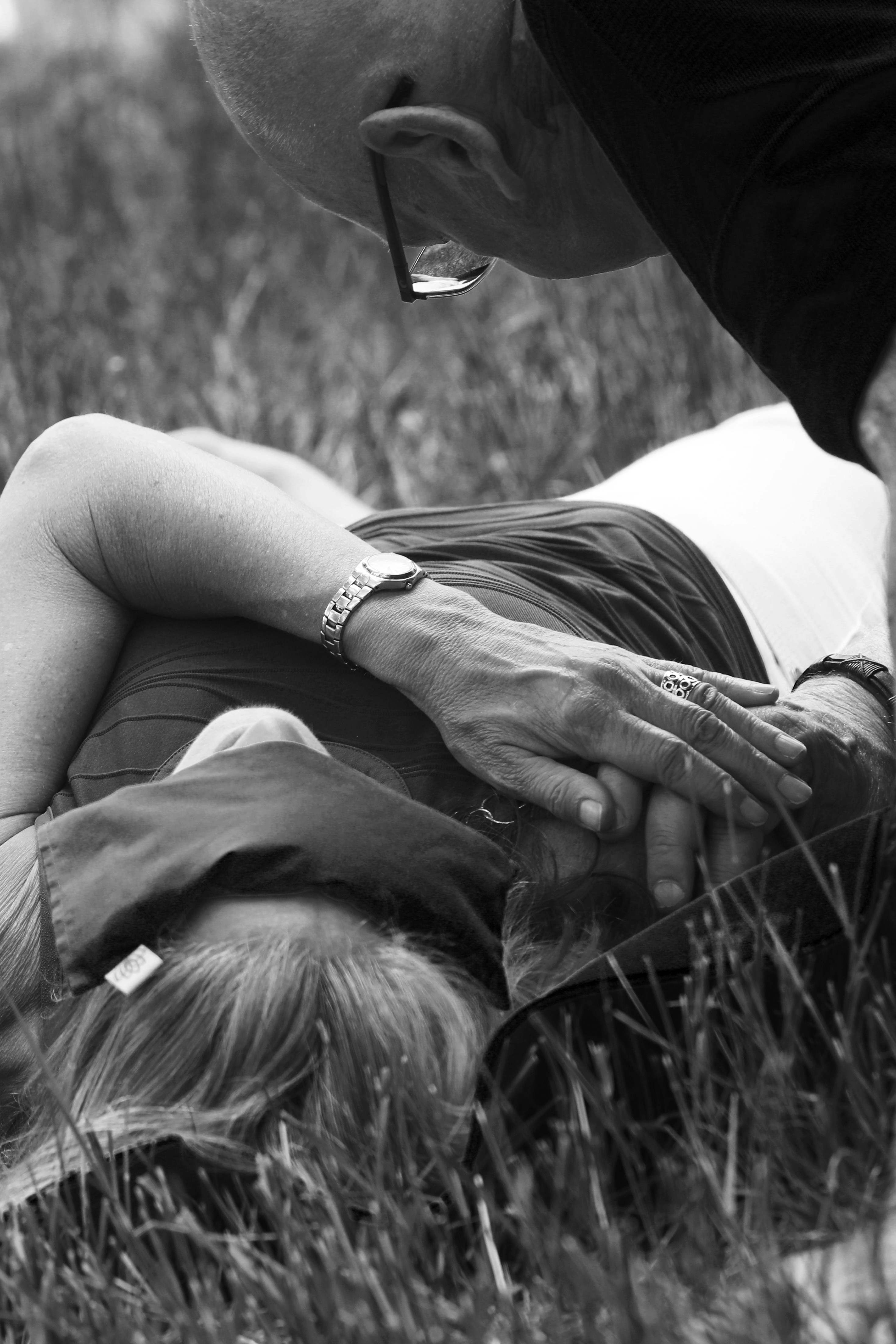 A person lying on grass with another person leaning over, holding their hand, in black and white.