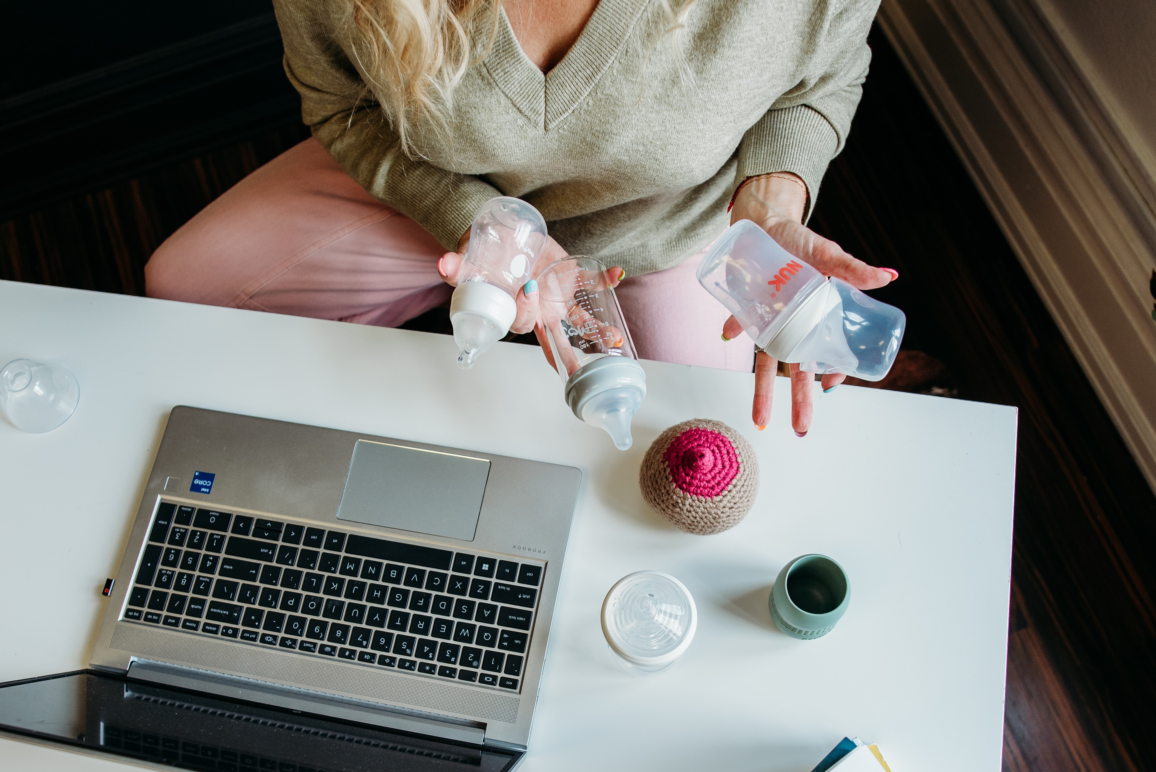 Person sitting at a desk with a laptop, holding water bottles, with a cupcake and cups on the table.