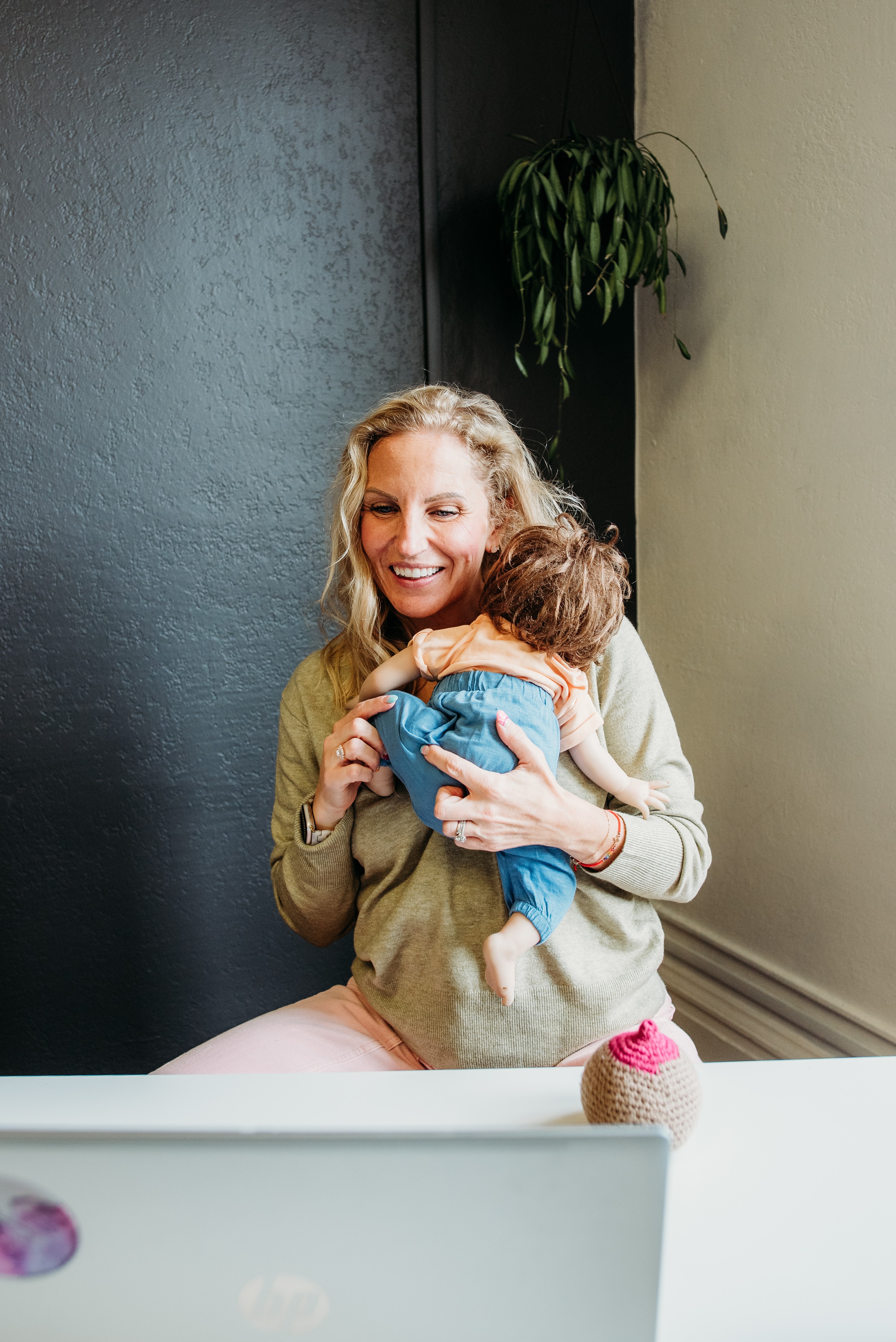 Woman smiling and hugging a child indoors near a black wall and a potted plant.