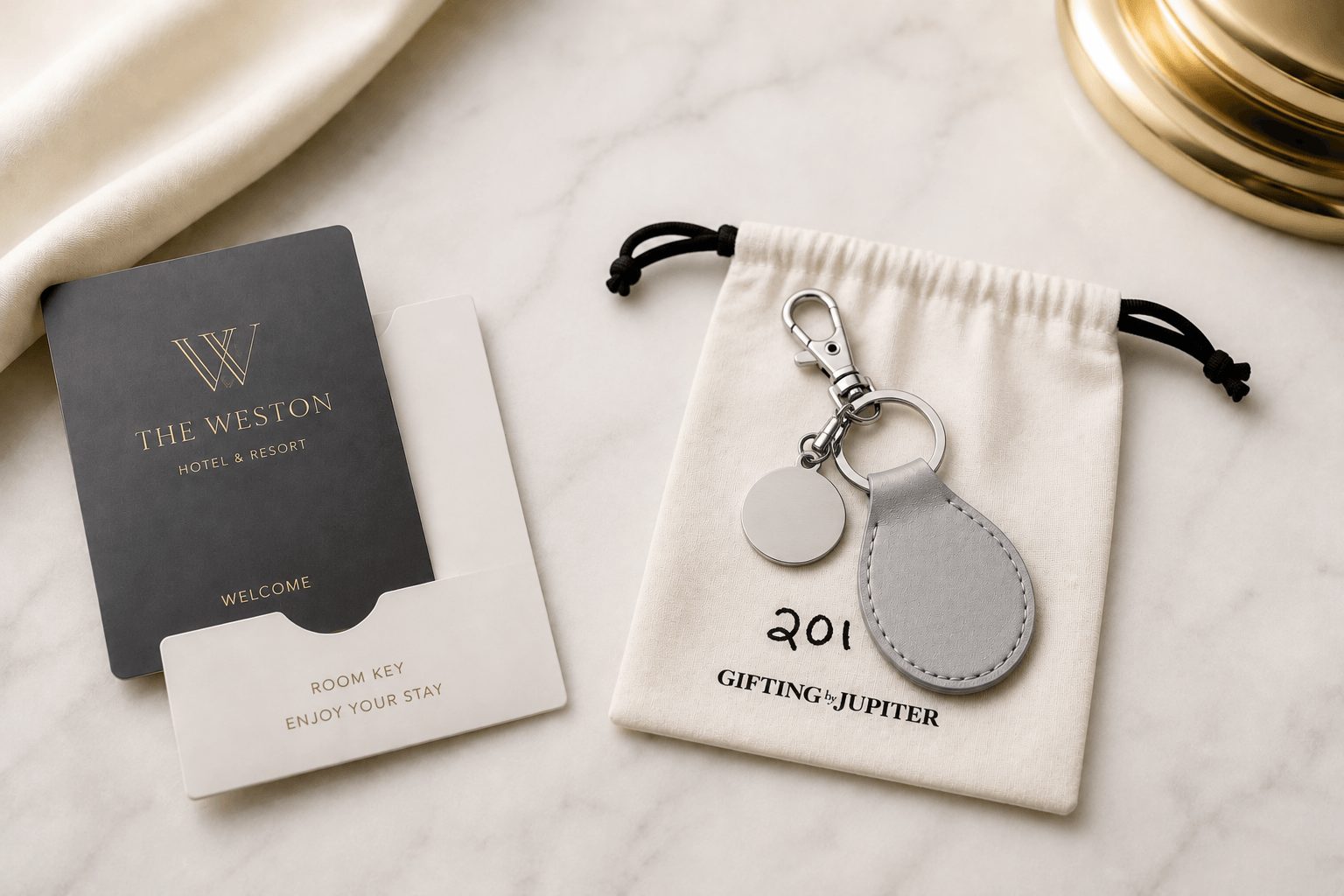 Black welcome card, keychain with gray leather pouch, and a small drawstring pouch on a marble surface.