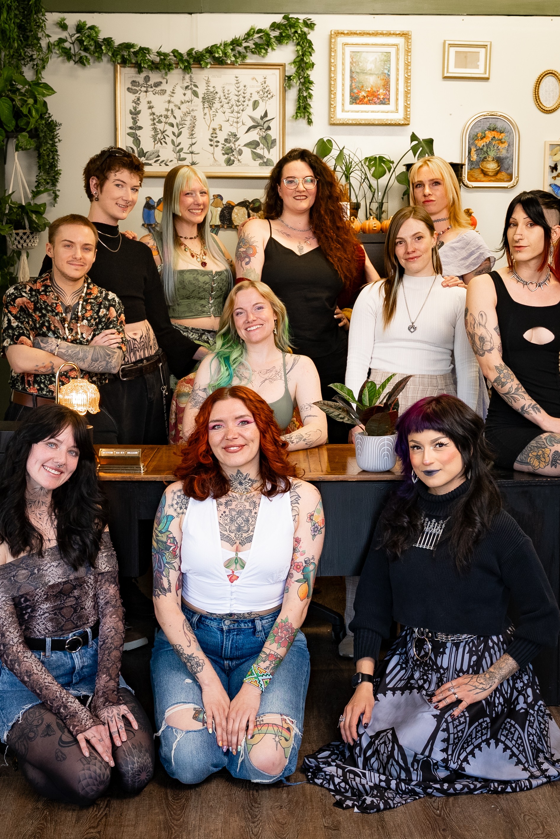Group of ten women posing indoors with plants and framed art on the wall behind them.