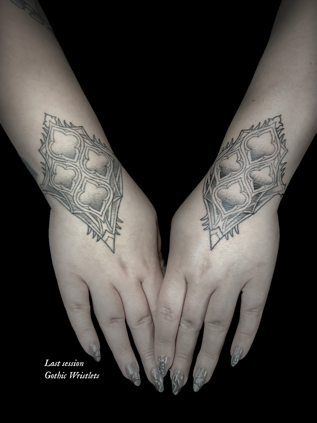 Two symmetrical geometric tattoos on wrists, black background, hands with painted nails, text at bottom left corner, 20 words.