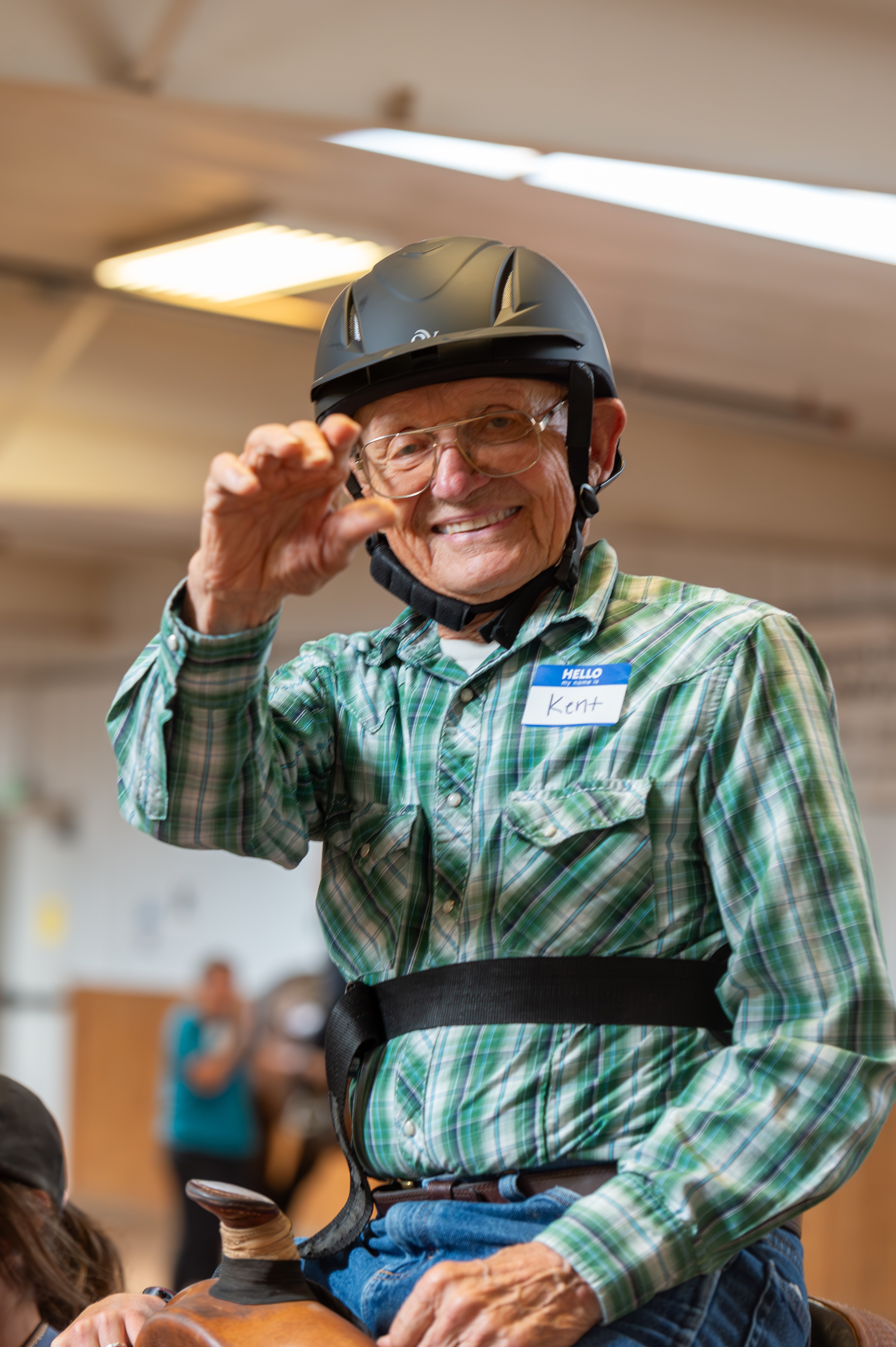 Smiling man wearing a helmet and glasses, adjusting his glasses with his right hand, in an indoor setting.