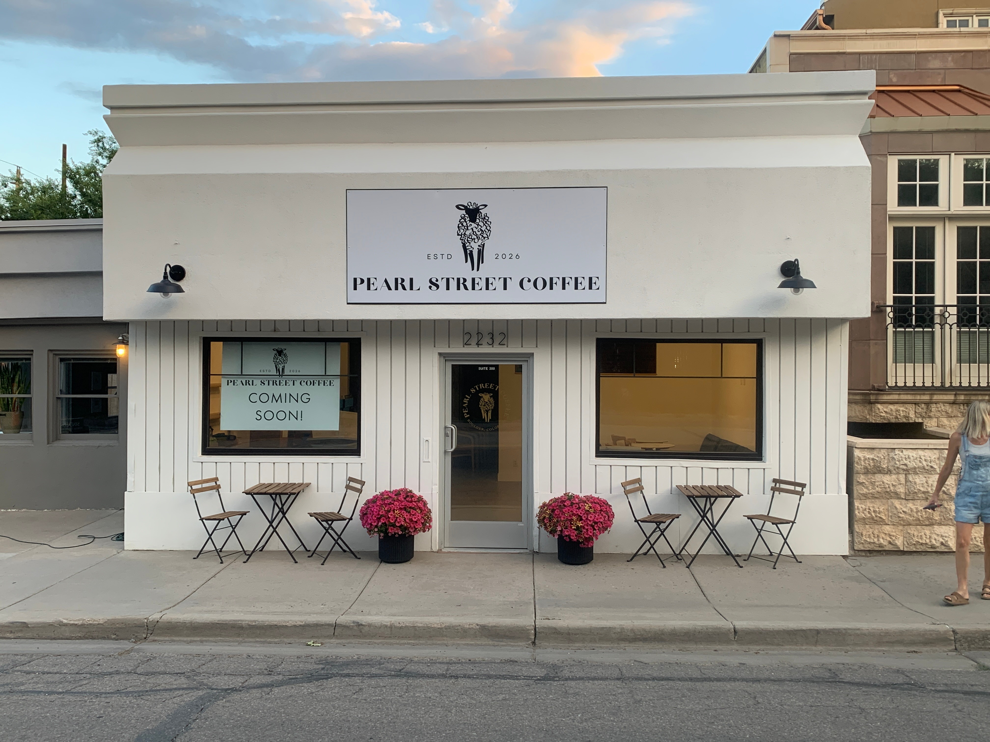 Coffee shop with white exterior, outdoor seating, and pink flowers outside, under a sign reading Pearl Street Coffee.